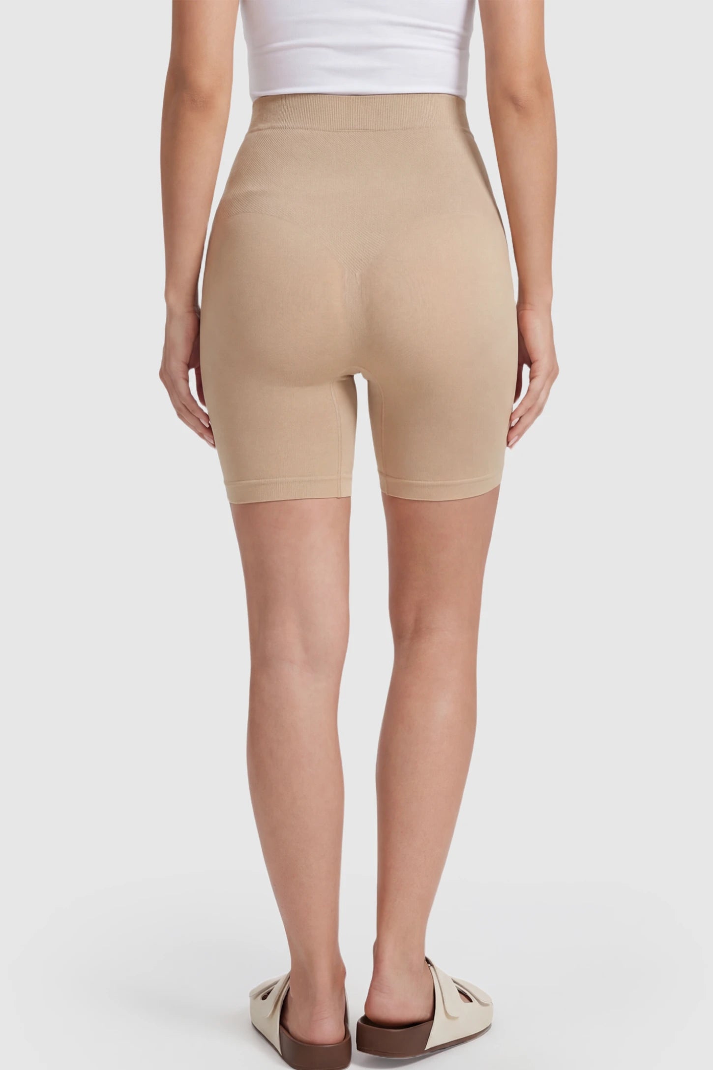 Seamless High Waisted Maternity Shapewear Shorts Seamless High-Waisted Mid Thigh Maternity Shapewear Shorts in Nude featuring a smooth belly support panel on a pregnant model showing back.