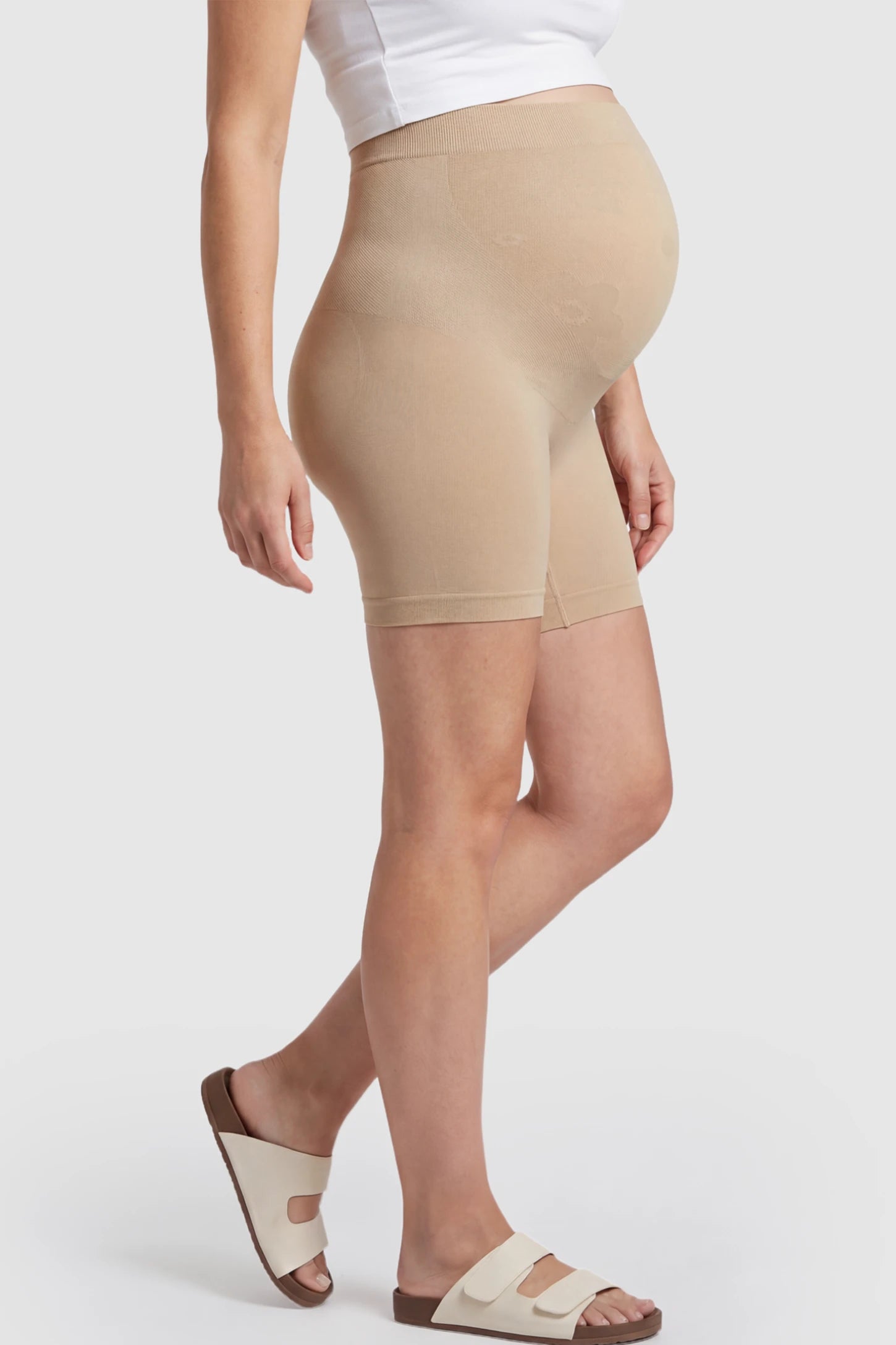 Seamless High Waisted Maternity Shapewear Shorts Seamless High-Waisted Mid Thigh Maternity Shapewear Shorts in Nude featuring a smooth belly support panel on a pregnant model showing side.