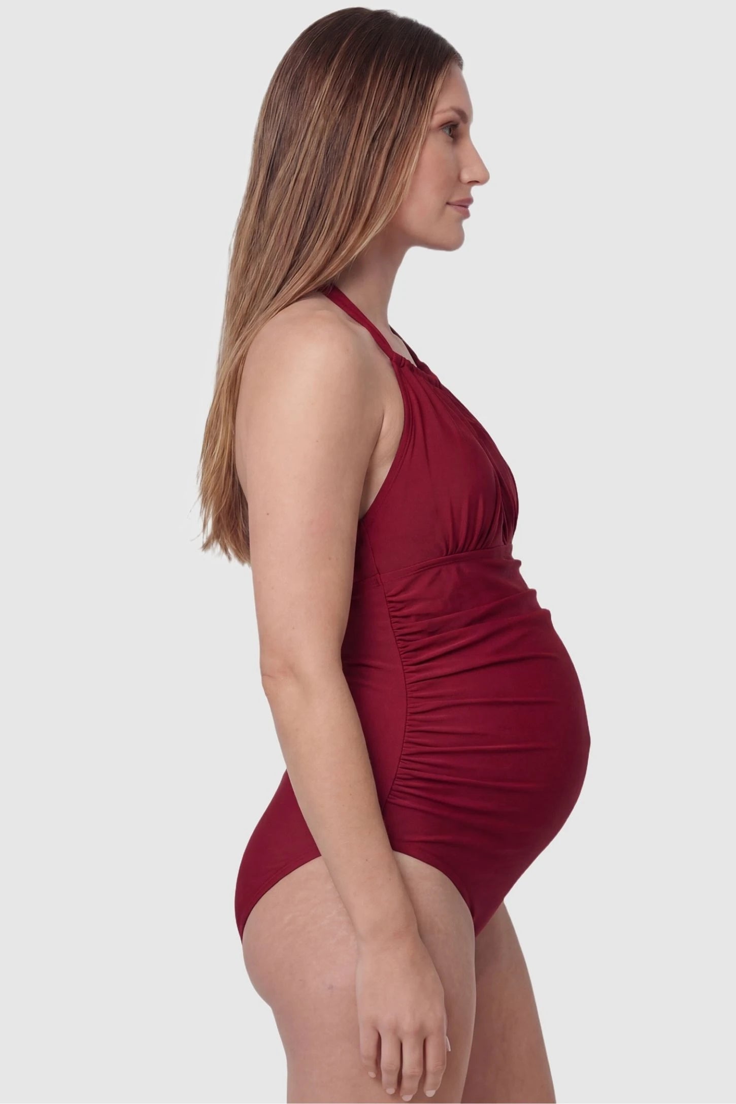Side-Ruched Halter Maternity One-Piece Side-Ruched Halter Maternity One-Piece in Red featuring flexible side-ruching for bump support on a pregnant model, side view.