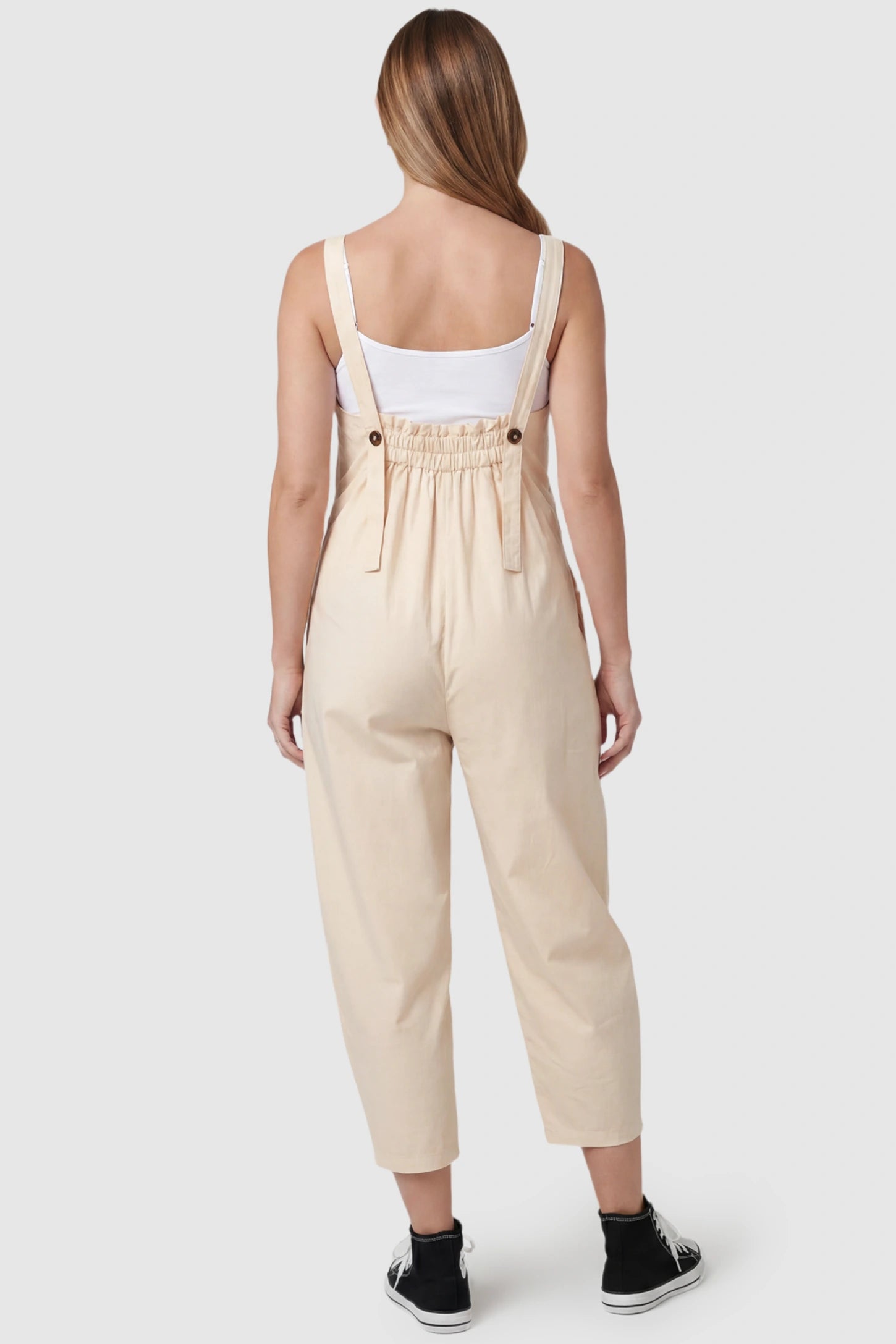 Sleeveless Balloon-Leg Maternity Jumpsuit Sleeveless Balloon-Leg Maternity Jumpsuit in Beige featuring an elasticated back and buttoned straps on a pregnant model, back view.