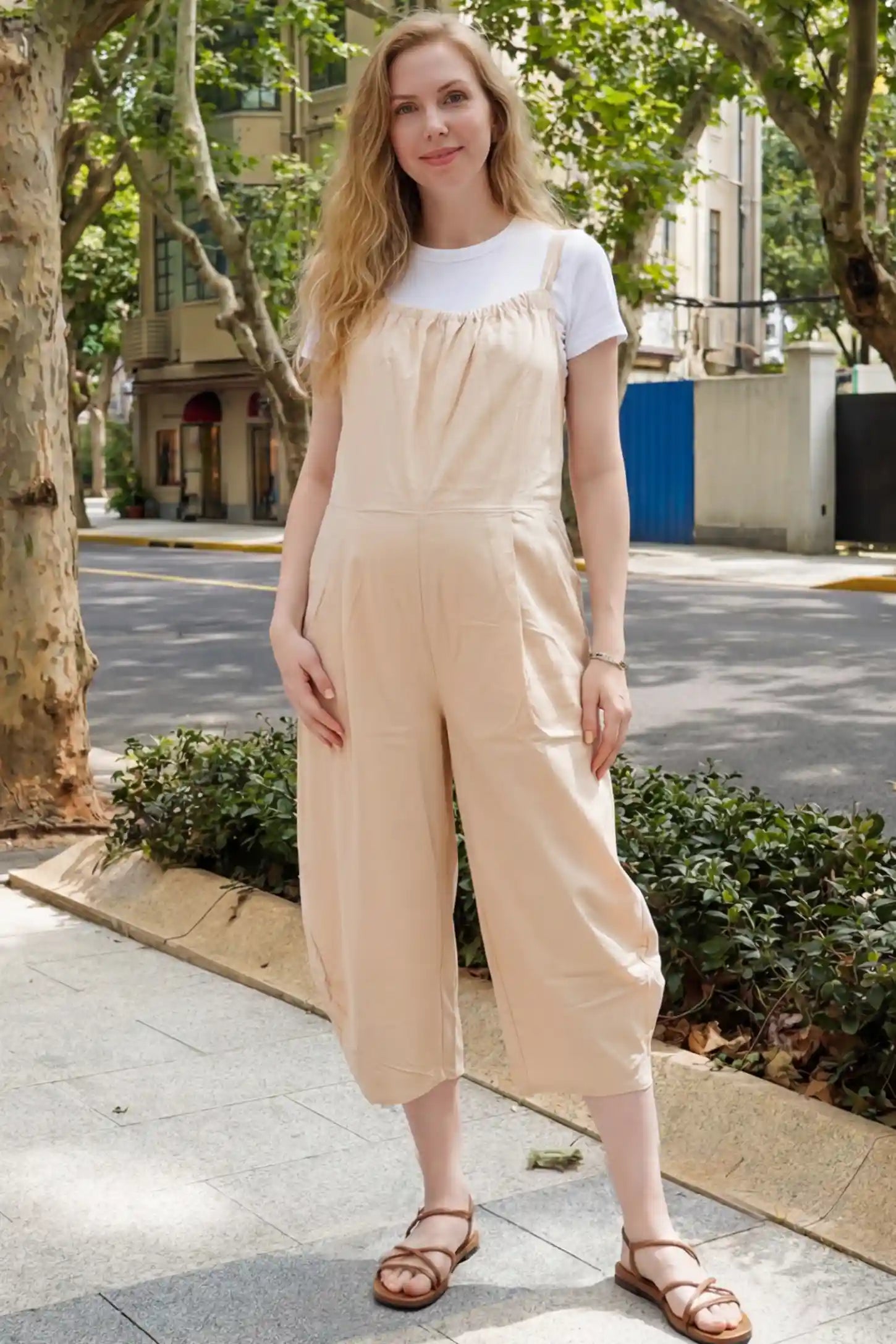 Sleeveless Balloon-Leg Maternity Jumpsuit Sleeveless Balloon-Leg Maternity Jumpsuit in Beige featuring deep side pockets on a pregnant woman standing on a city sidewalk.
