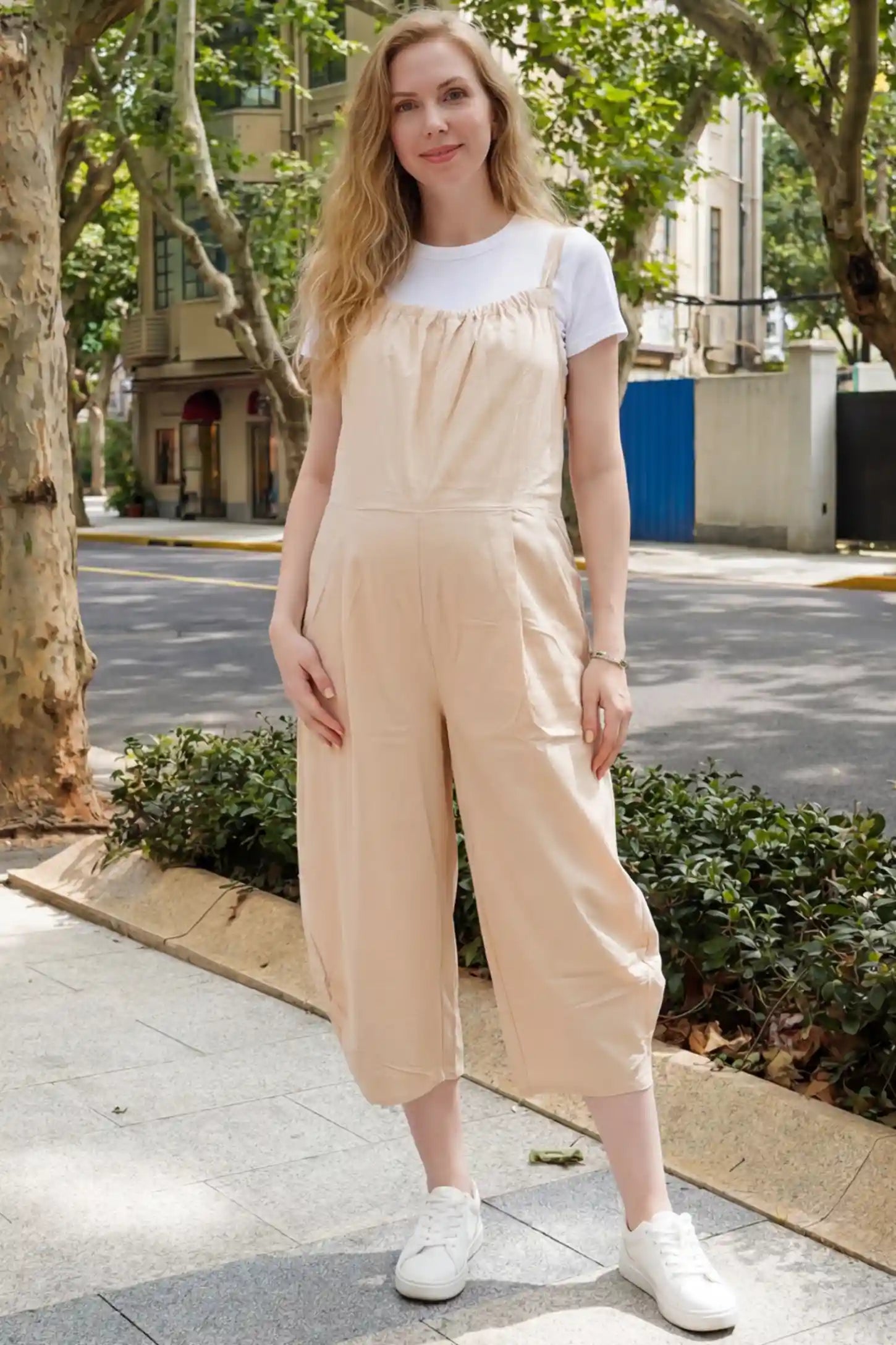 Sleeveless Balloon-Leg Maternity Jumpsuit Sleeveless Balloon-Leg Maternity Jumpsuit in Beige featuring deep side pockets on a pregnant woman in outdoor setting, front view.