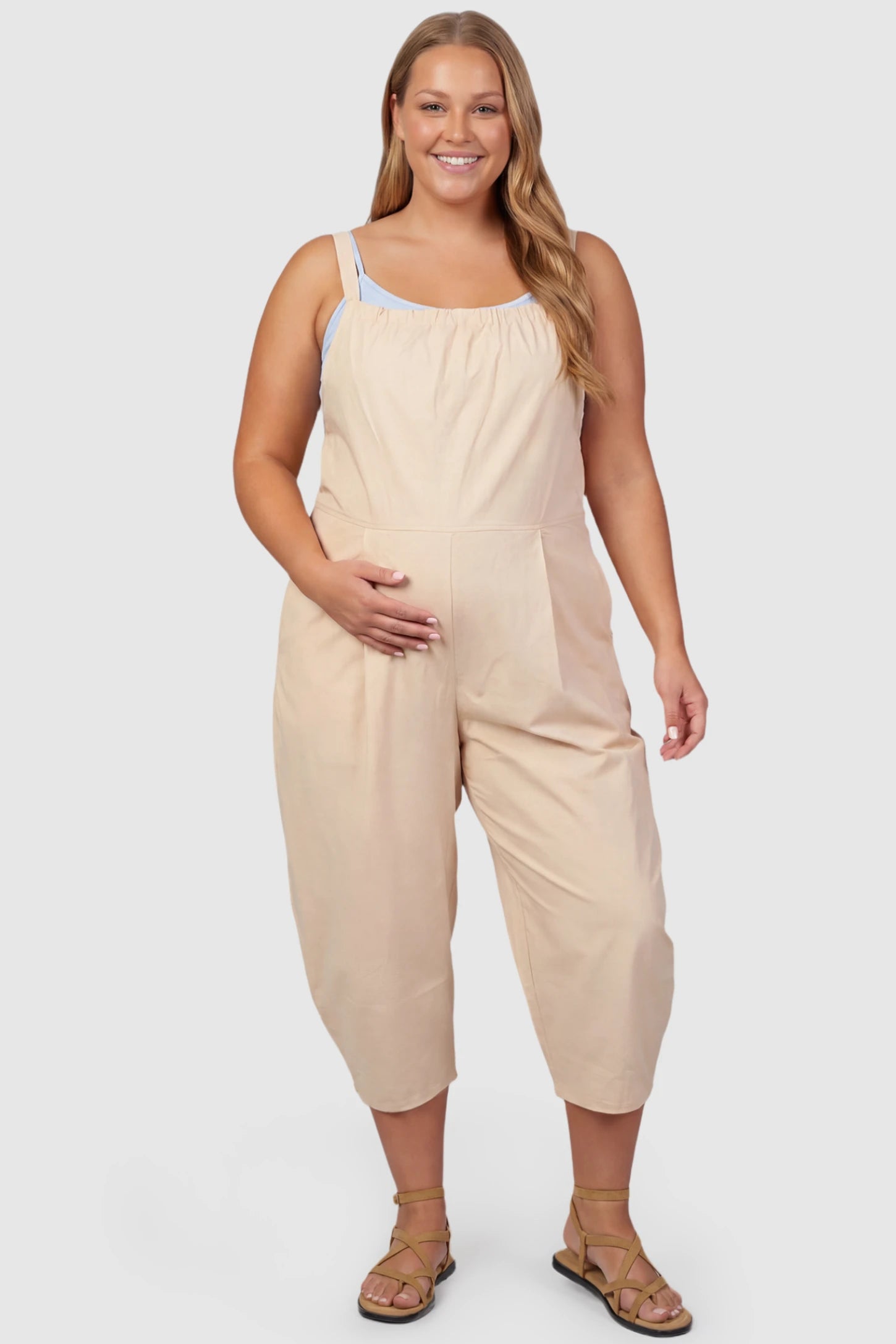 Sleeveless Balloon-Leg Maternity Jumpsuit Sleeveless Balloon-Leg Maternity Jumpsuit in Beige featuring deep side pockets on a plus size pregnant model, front view.