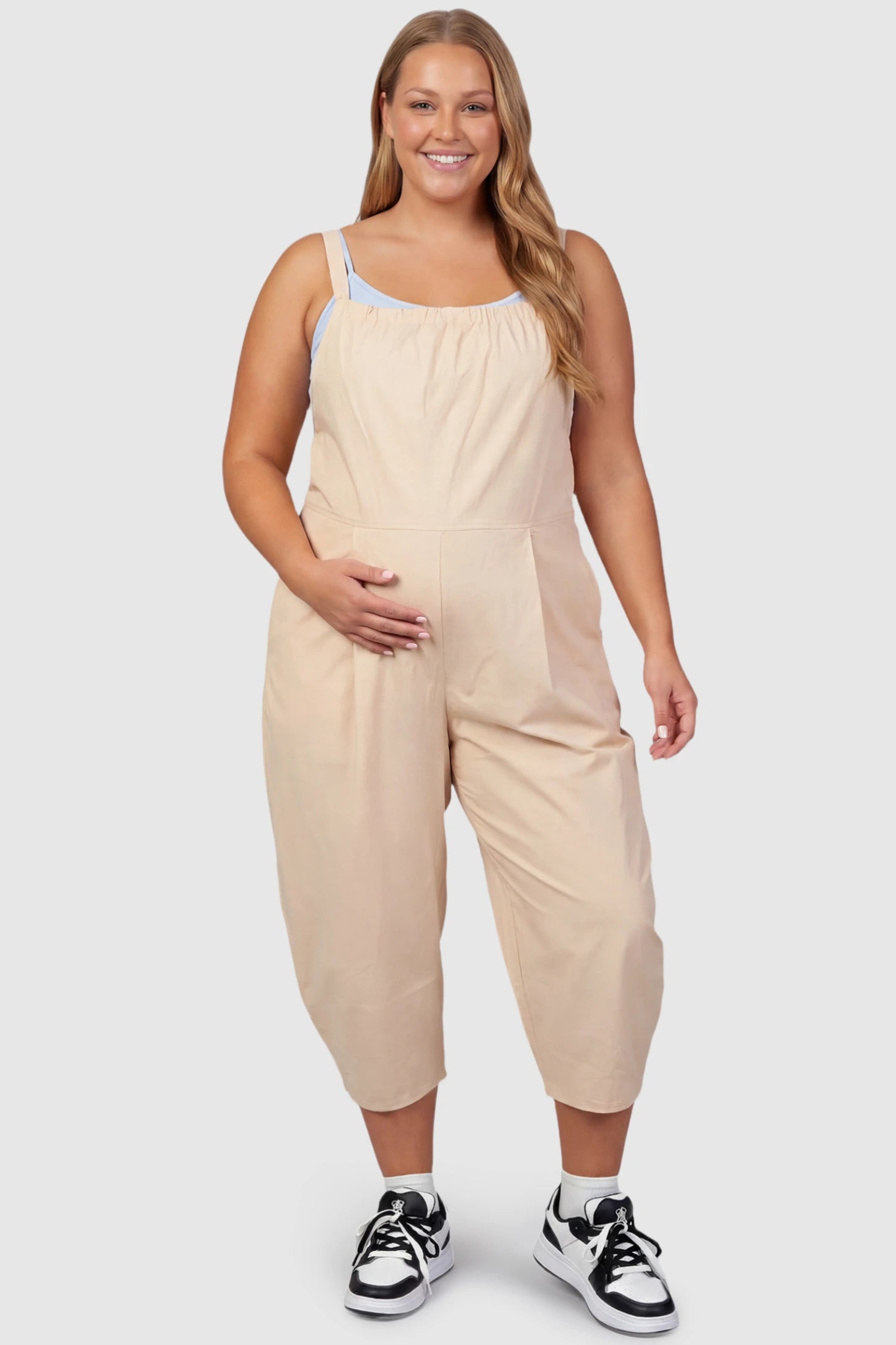 Sleeveless Balloon-Leg Maternity Jumpsuit Sleeveless Balloon-Leg Maternity Jumpsuit in Beige featuring deep side pockets on a plus size pregnant model, front view.
