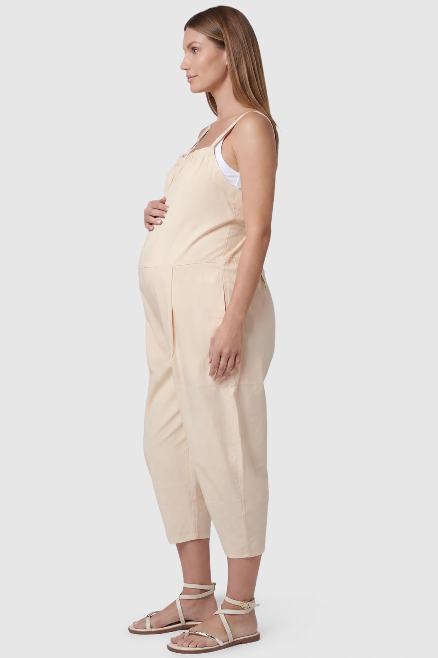 Sleeveless Balloon-Leg Maternity Jumpsuit Sleeveless Balloon-Leg Maternity Jumpsuit in Beige featuring deep side pockets on a pregnant model, side view.