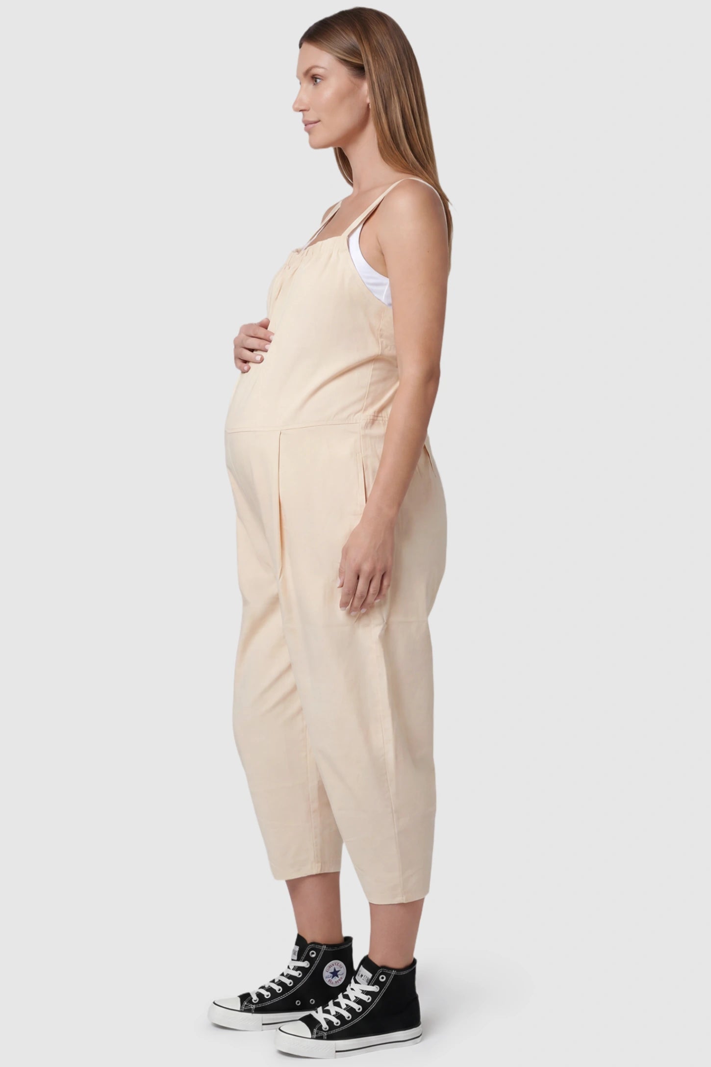 Sleeveless Balloon-Leg Maternity Jumpsuit Sleeveless Balloon-Leg Maternity Jumpsuit in Beige featuring deep side pockets on a pregnant model, side view.