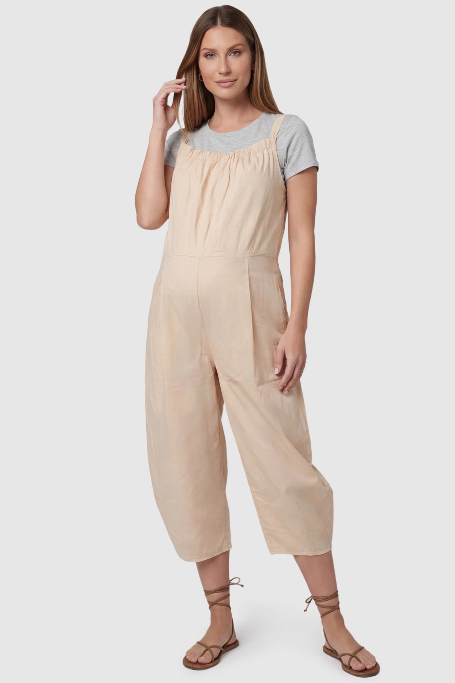Sleeveless Balloon-Leg Maternity Jumpsuit in Beige featuring deep side pockets on a pregnant model, front view.