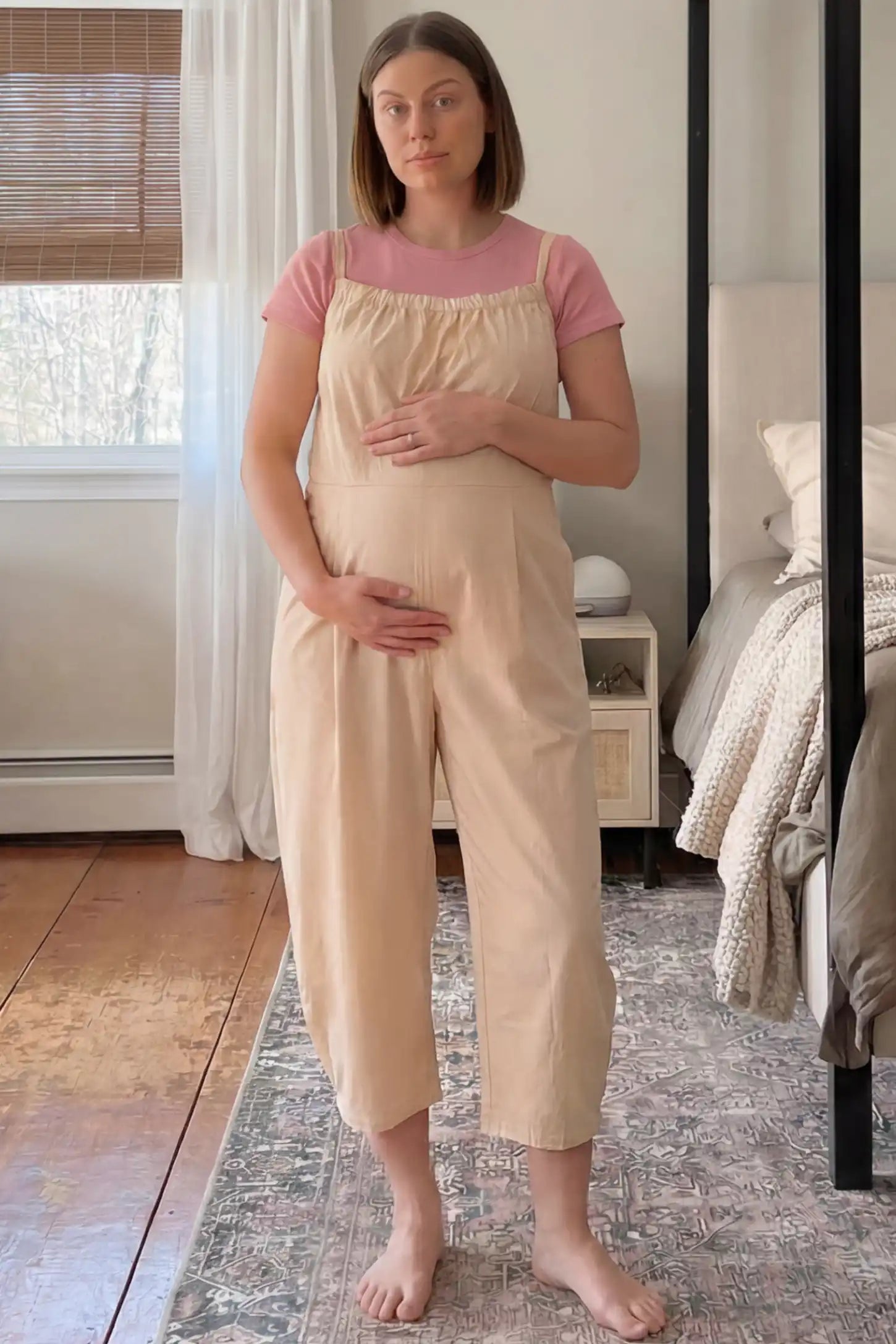 Sleeveless Balloon-Leg Maternity Jumpsuit Sleeveless Balloon-Leg Maternity Jumpsuit in Beige featuring deep side pockets on a pregnant woman standing in a bedroom setting.