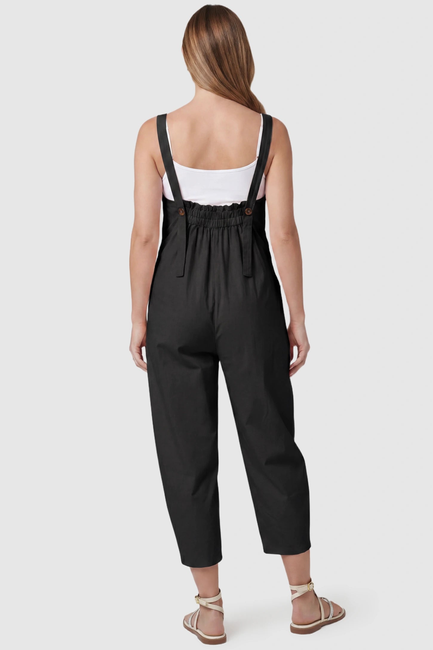 Sleeveless Balloon-Leg Maternity Jumpsuit Sleeveless Balloon-Leg Maternity Jumpsuit in Black featuring an elasticated back and buttoned straps on a pregnant model, back view.