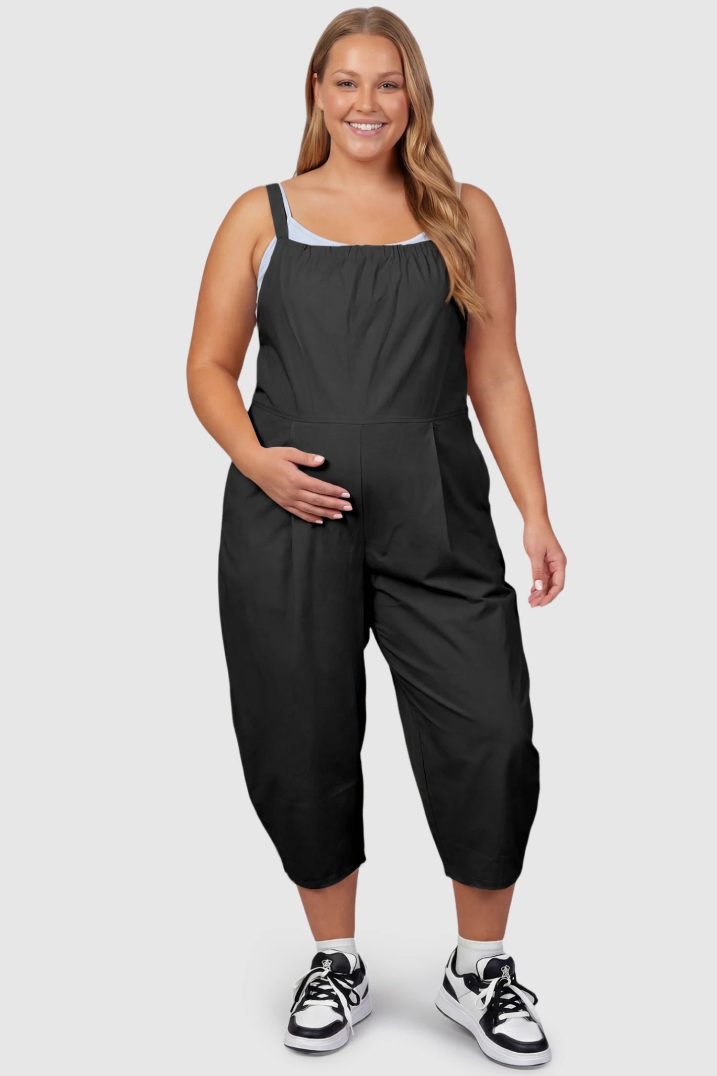 Sleeveless Balloon-Leg Maternity Jumpsuit Sleeveless Balloon-Leg Maternity Jumpsuit in Black featuring deep side pockets on a plus size pregnant model, front view.