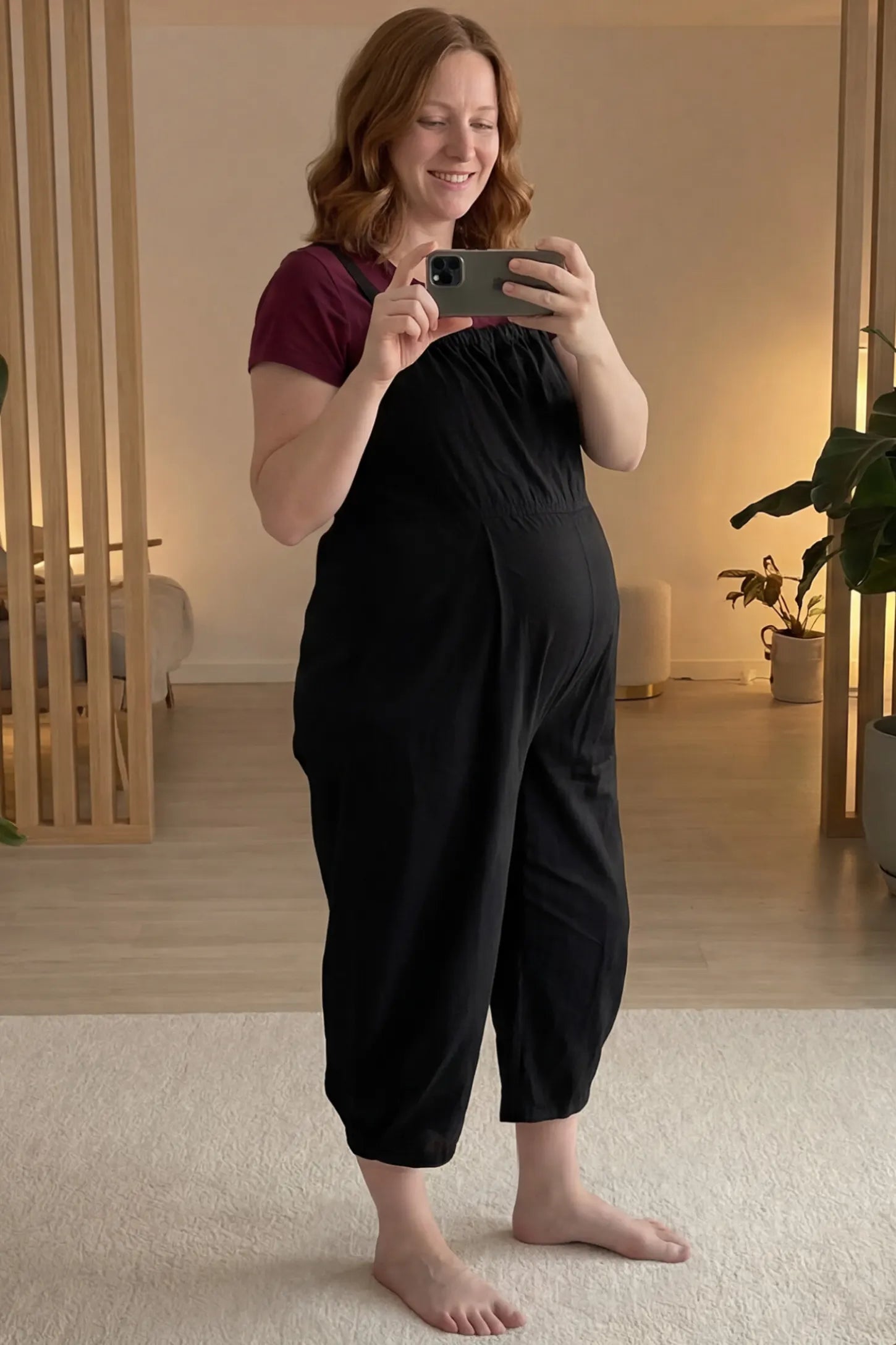 Sleeveless Balloon-Leg Maternity Jumpsuit Sleeveless Balloon-Leg Maternity Jumpsuit in Black featuring deep side pockets on a pregnant woman taking a mirror selfie in a home setting.