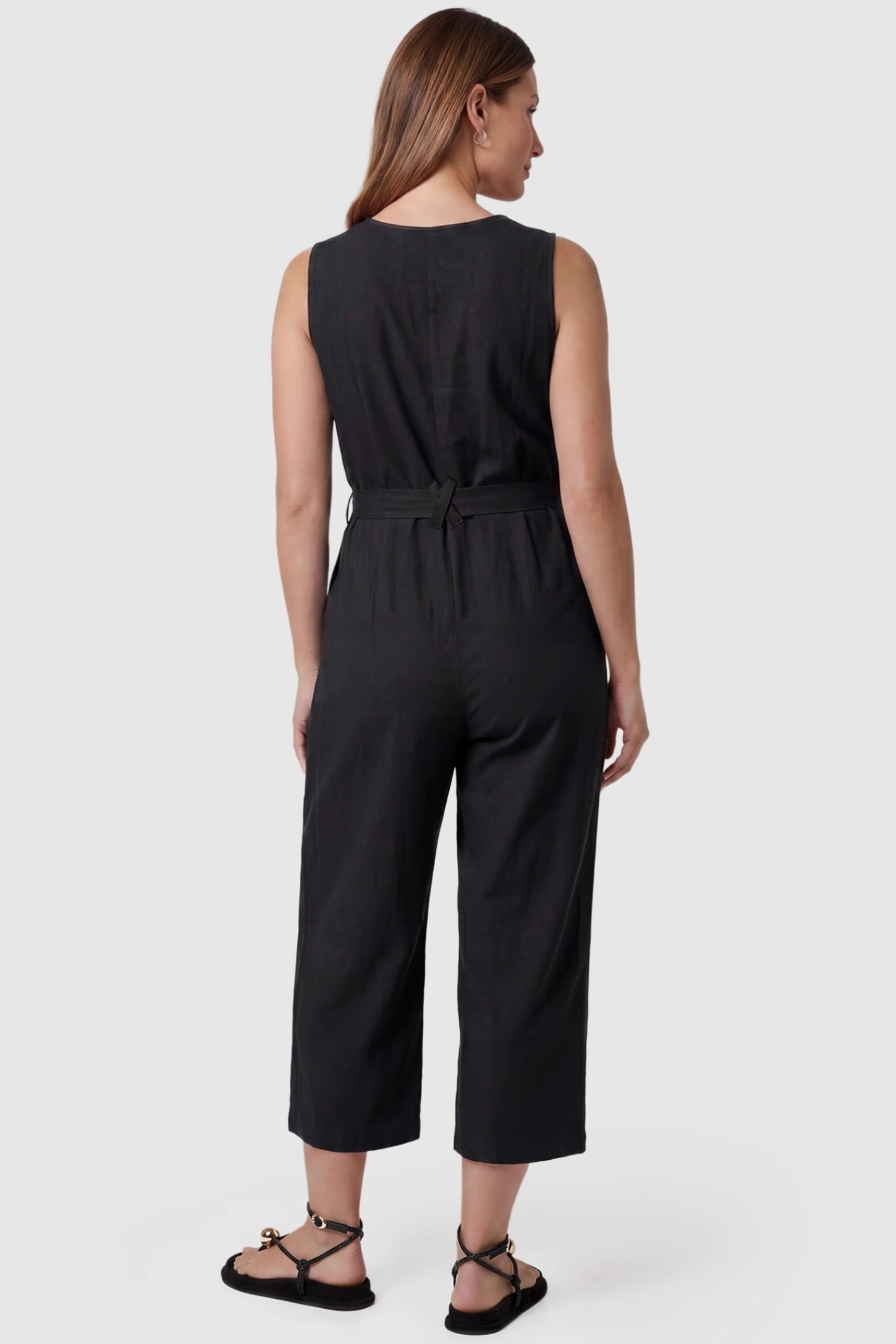 Sleeveless V-Neck Tie-Waist Maternity Jumpsuit Sleeveless V-Neck Tie-Waist Maternity Jumpsuit in Black featuring a relaxed wide-leg design on a pregnant model, back view.