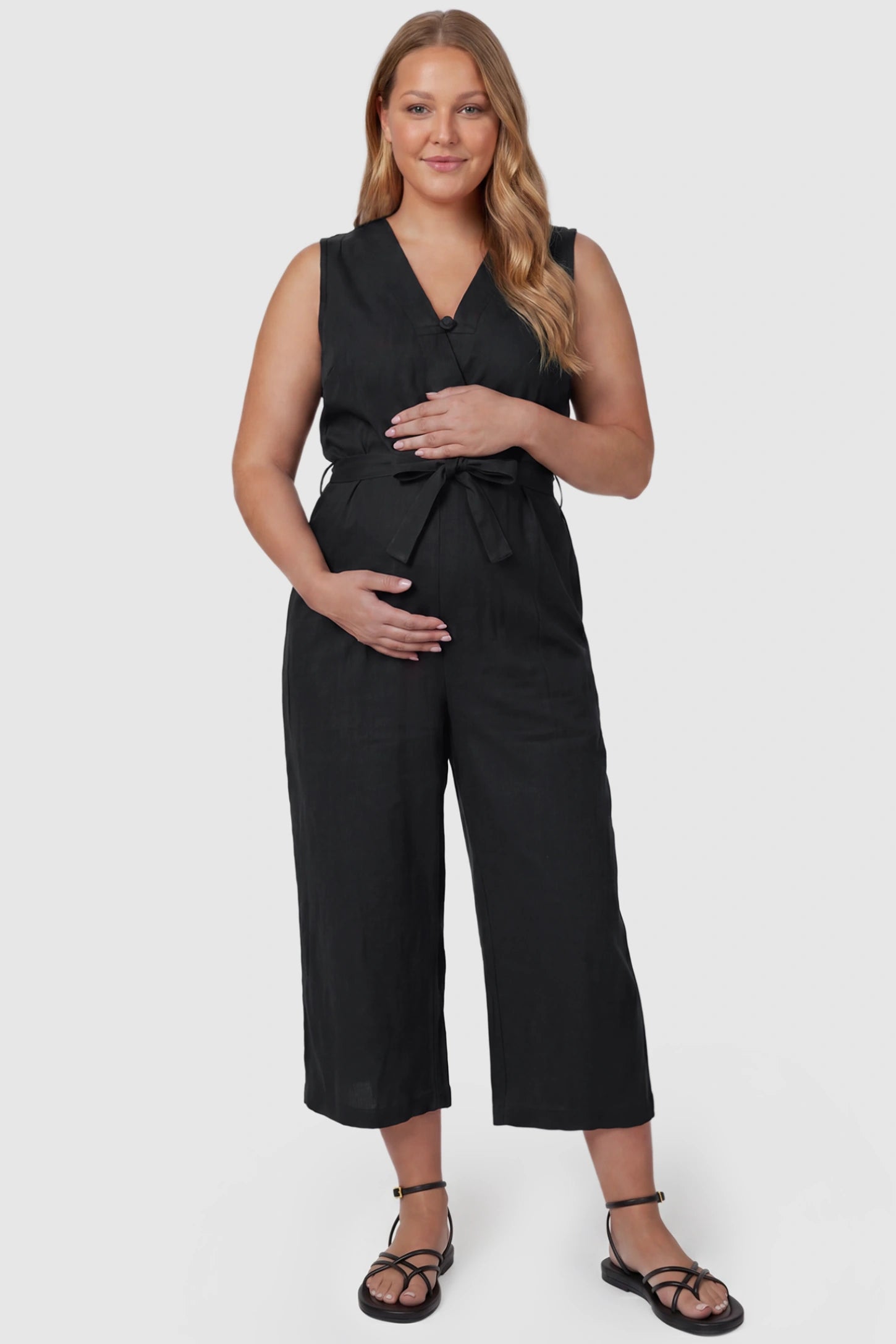 Sleeveless V-Neck Tie-Waist Maternity Jumpsuit Sleeveless V-Neck Tie-Waist Maternity Jumpsuit in Black featuring a relaxed wide-leg design on a plus size pregnant model, front view.
