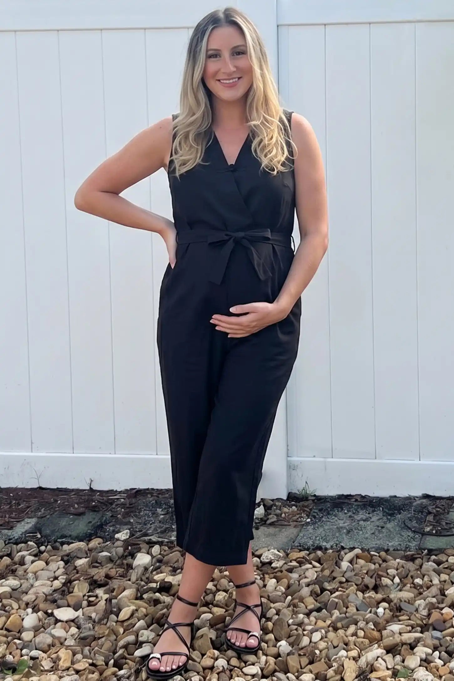 Sleeveless V-Neck Tie-Waist Maternity Jumpsuit Sleeveless V-Neck Tie-Waist Maternity Jumpsuit in Black featuring a relaxed wide-leg design on a pregnant woman in outdoor setting, front view.