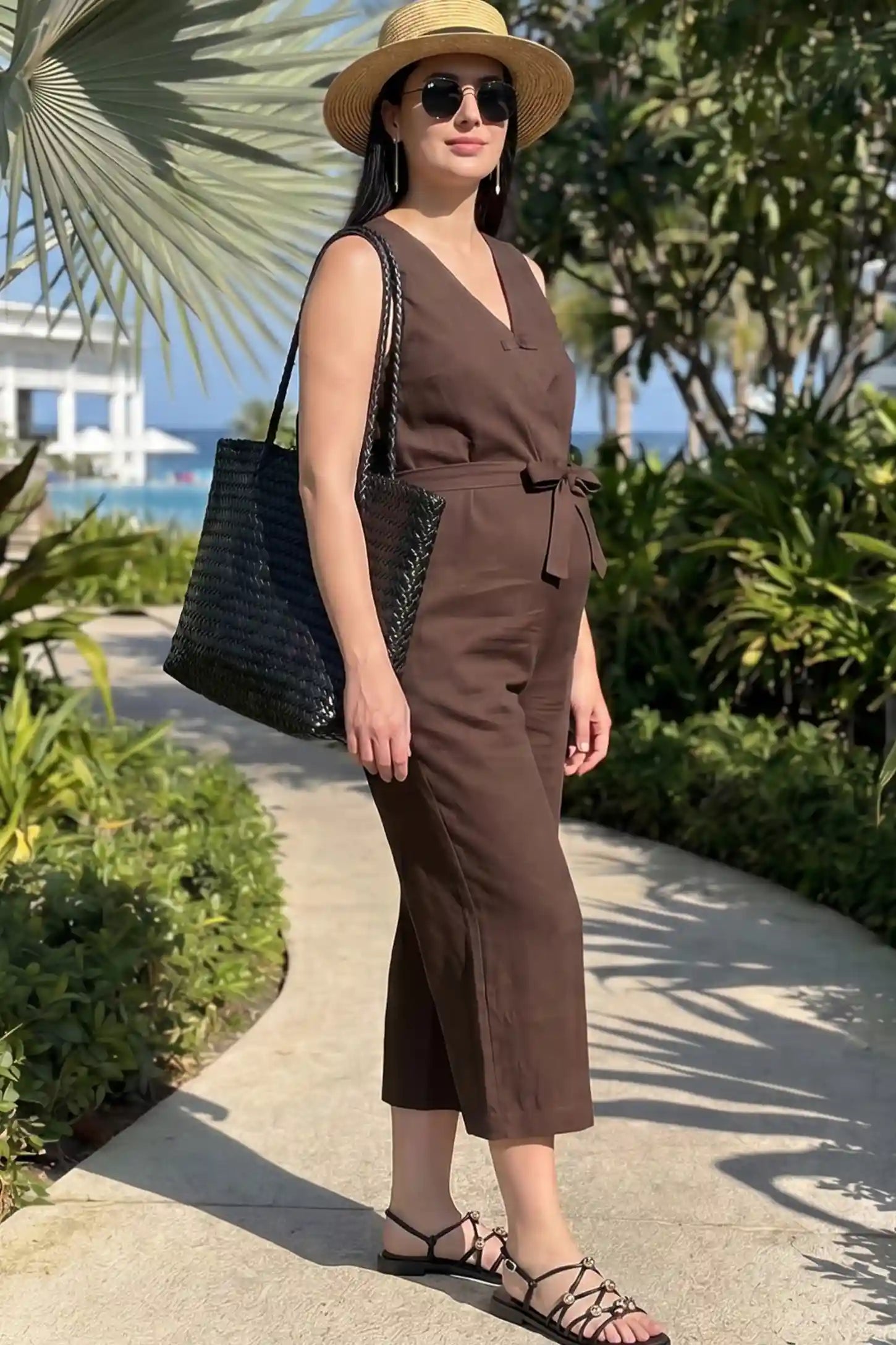 Sleeveless V-Neck Tie-Waist Maternity Jumpsuit Sleeveless V-Neck Tie-Waist Maternity Jumpsuit in Brown featuring a relaxed wide-leg design on a pregnant woman in outdoor setting, side view.