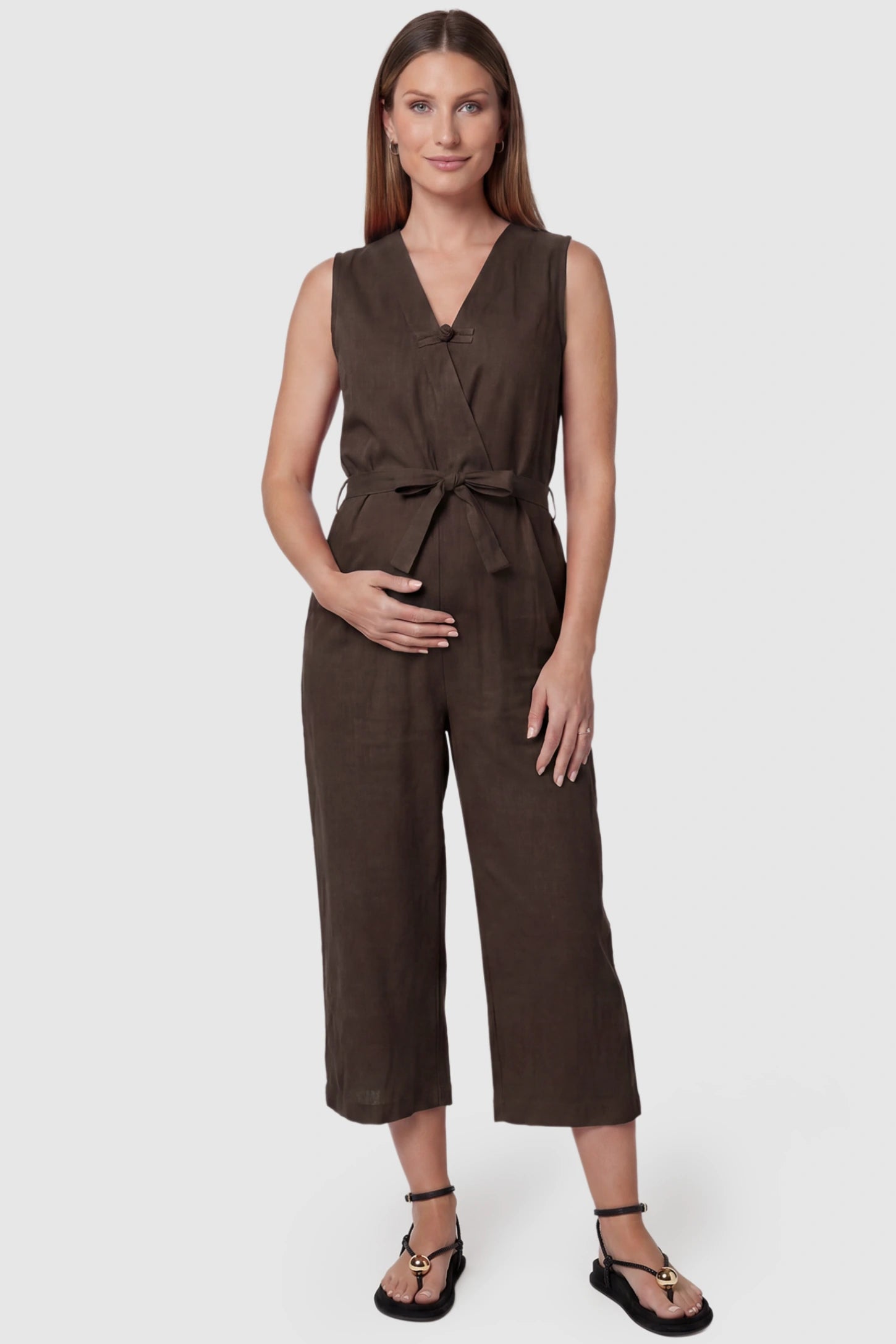 Sleeveless V-Neck Tie-Waist Maternity Jumpsuit Sleeveless V-Neck Tie-Waist Maternity Jumpsuit in Brown featuring a relaxed wide-leg design on a pregnant model, front view.