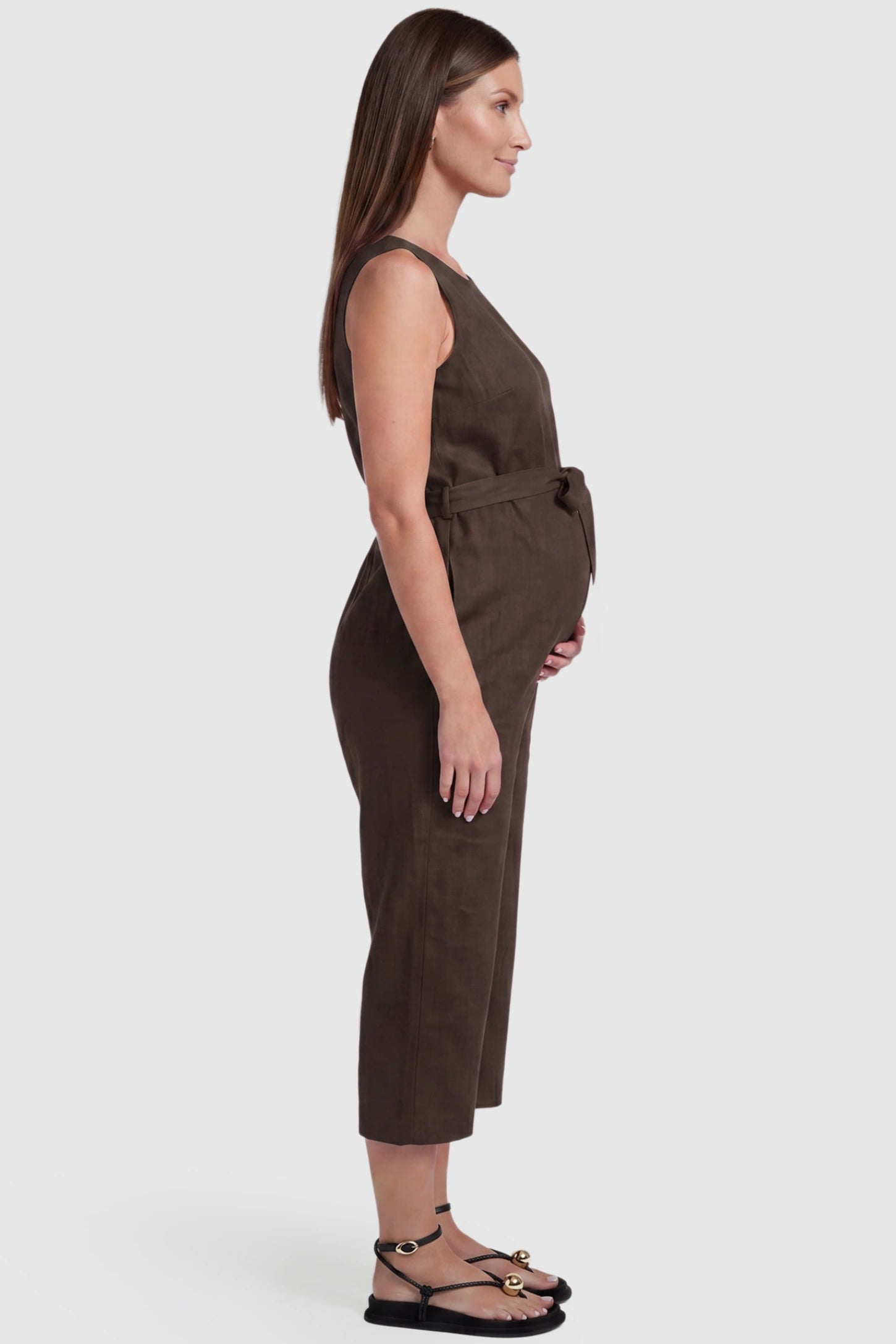 Sleeveless V-Neck Tie-Waist Maternity Jumpsuit Sleeveless V-Neck Tie-Waist Maternity Jumpsuit in Brown featuring a relaxed wide-leg design on a pregnant model, side view.