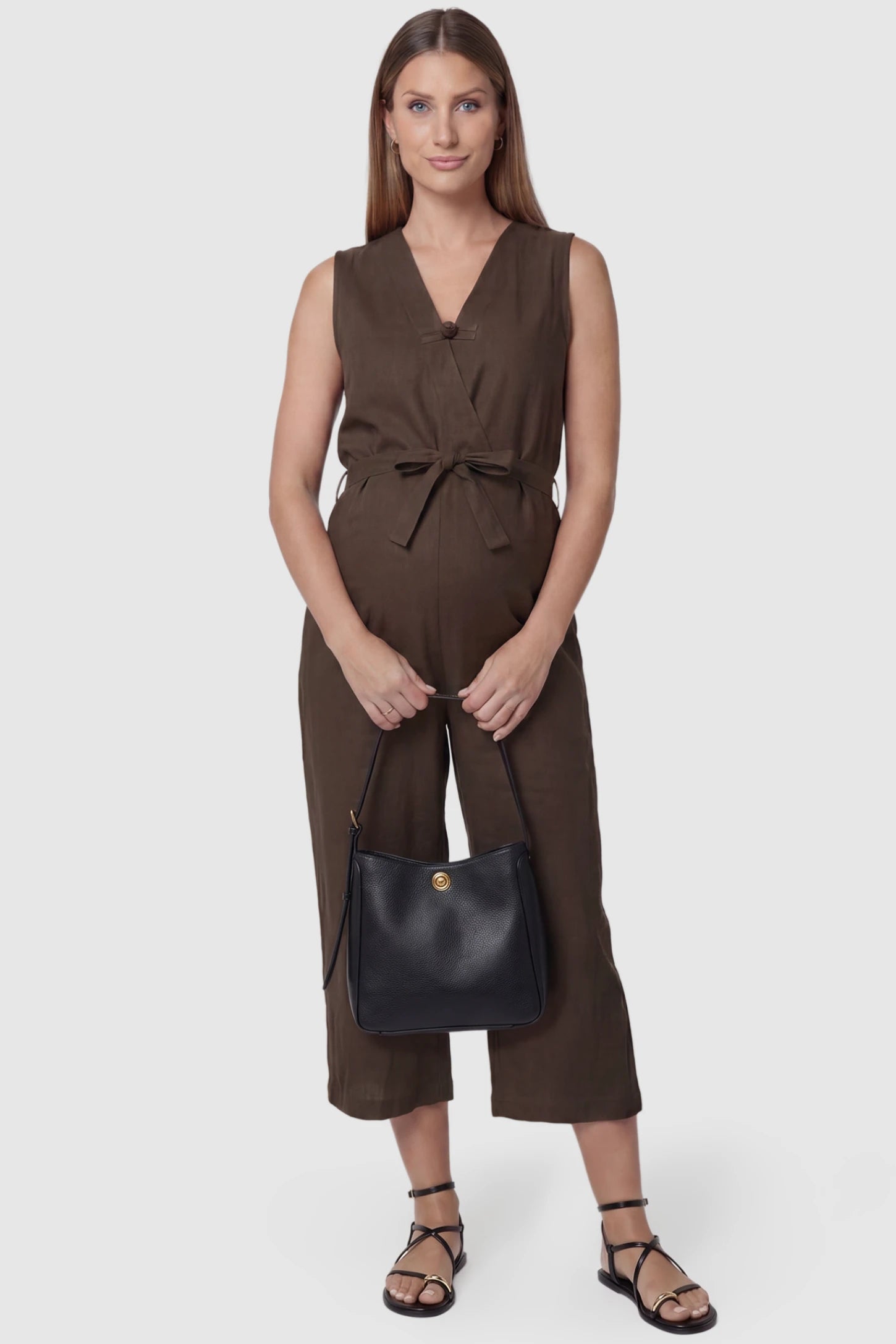 Sleeveless V-Neck Tie-Waist Maternity Jumpsuit Sleeveless V-Neck Tie-Waist Maternity Jumpsuit in Brown featuring a relaxed wide-leg design on a pregnant model, front view.