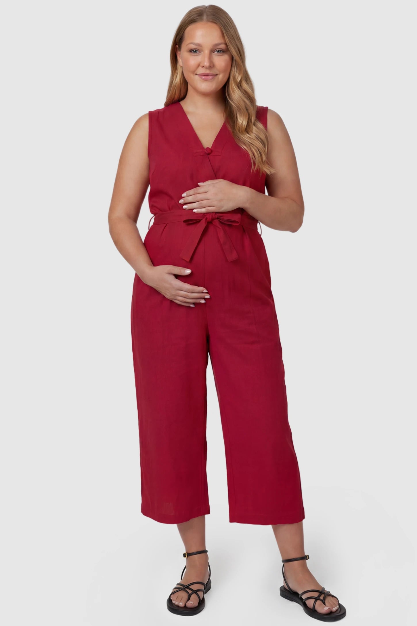 Sleeveless V-Neck Tie-Waist Maternity Jumpsuit Sleeveless V-Neck Tie-Waist Maternity Jumpsuit in Red featuring a relaxed wide-leg design on a plus size pregnant model, front view.