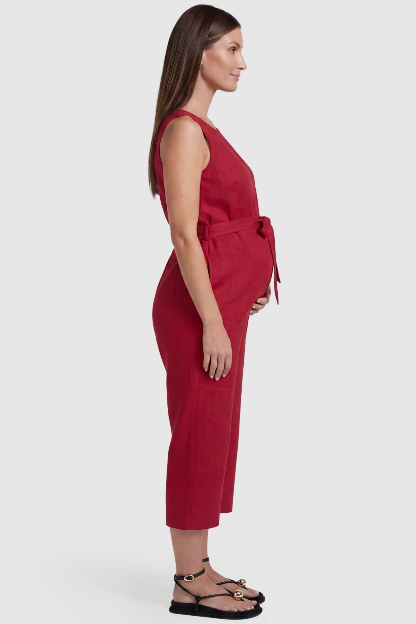 Sleeveless V-Neck Tie-Waist Maternity Jumpsuit Sleeveless V-Neck Tie-Waist Maternity Jumpsuit in Red featuring a relaxed wide-leg design on a pregnant model, side view.