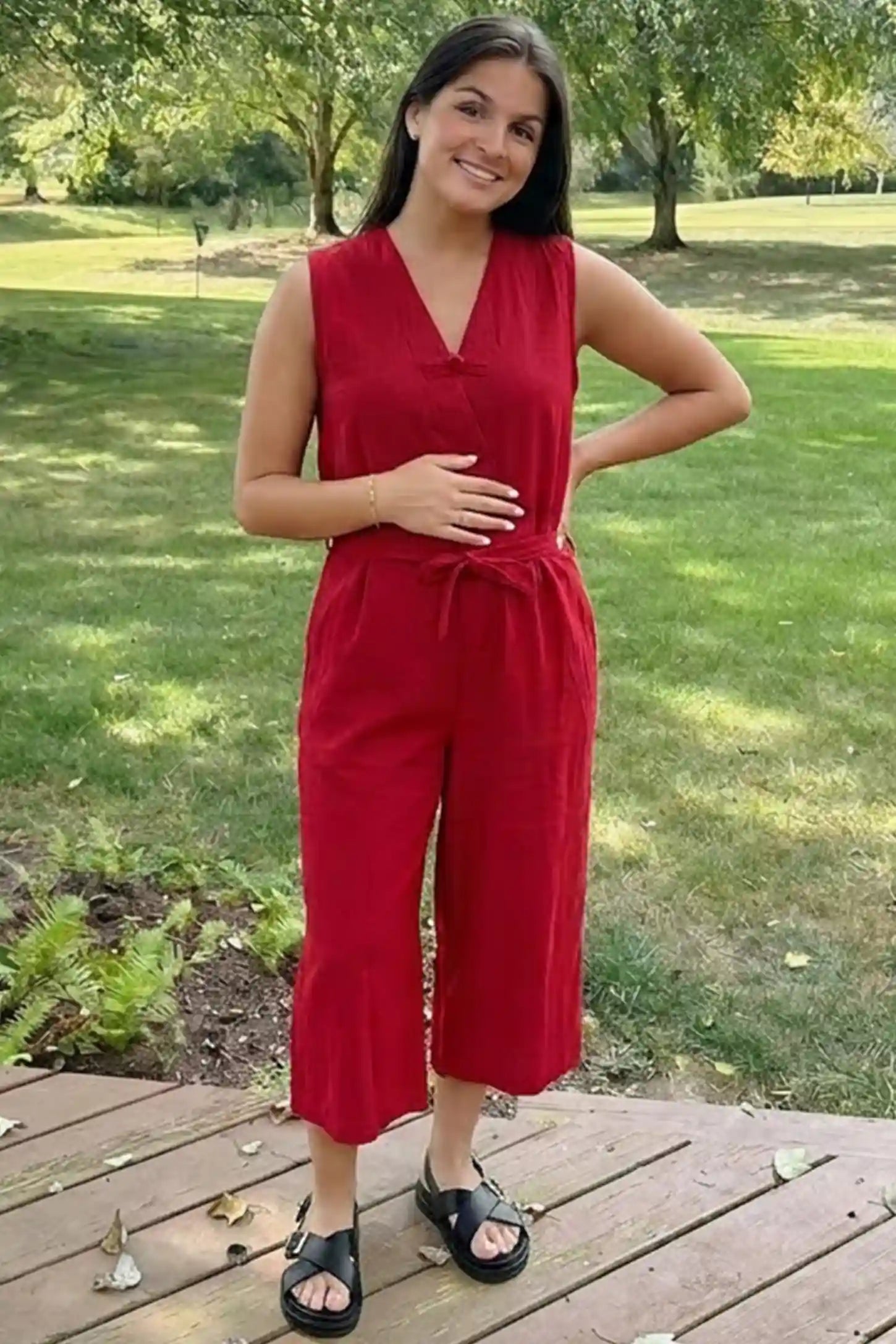 Sleeveless V-Neck Tie-Waist Maternity Jumpsuit Sleeveless V-Neck Tie-Waist Maternity Jumpsuit in Red featuring a relaxed wide-leg design on a pregnant woman in outdoor setting, front view.