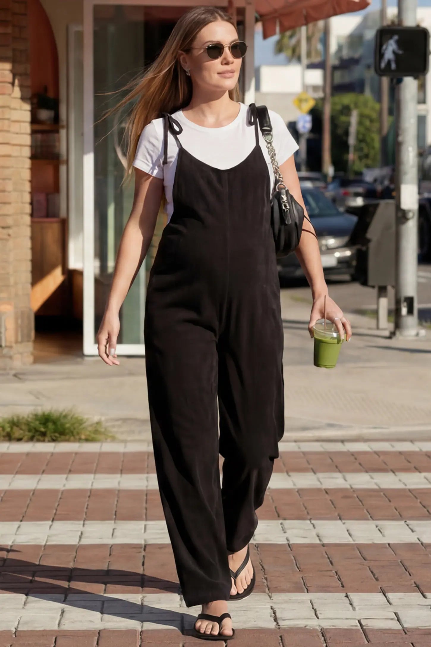 Solid Sleeveless Wide Leg Maternity Jumpsuit Solid Sleeveless Wide Leg Maternity Jumpsuit in Black featuring a flowy silhouette on a pregnant woman in an outdoor setting, front view.
