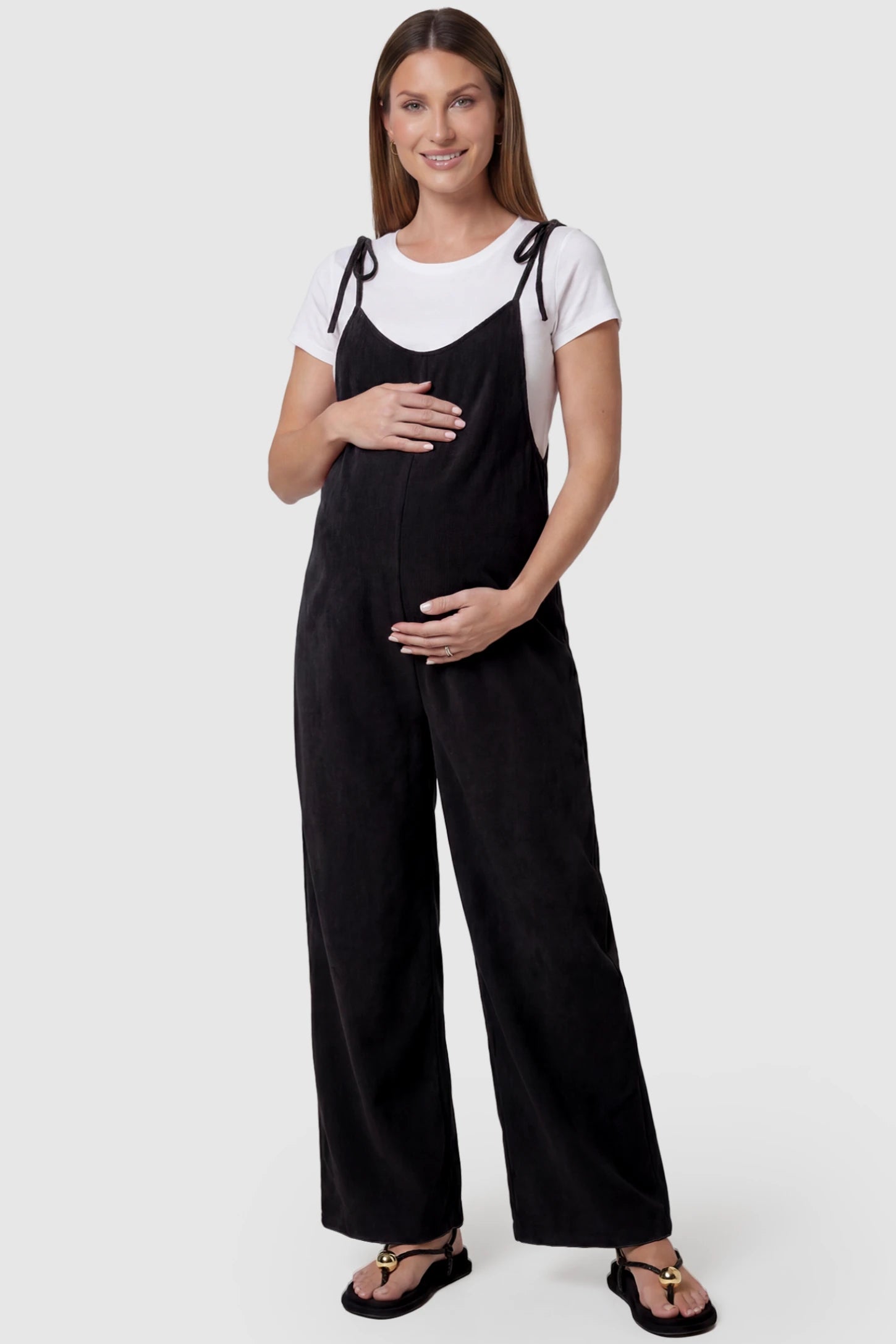 Solid Sleeveless Wide Leg Maternity Jumpsuit Solid Sleeveless Wide Leg Maternity Jumpsuit in Black featuring a flowy silhouette on a pregnant model, front view.
