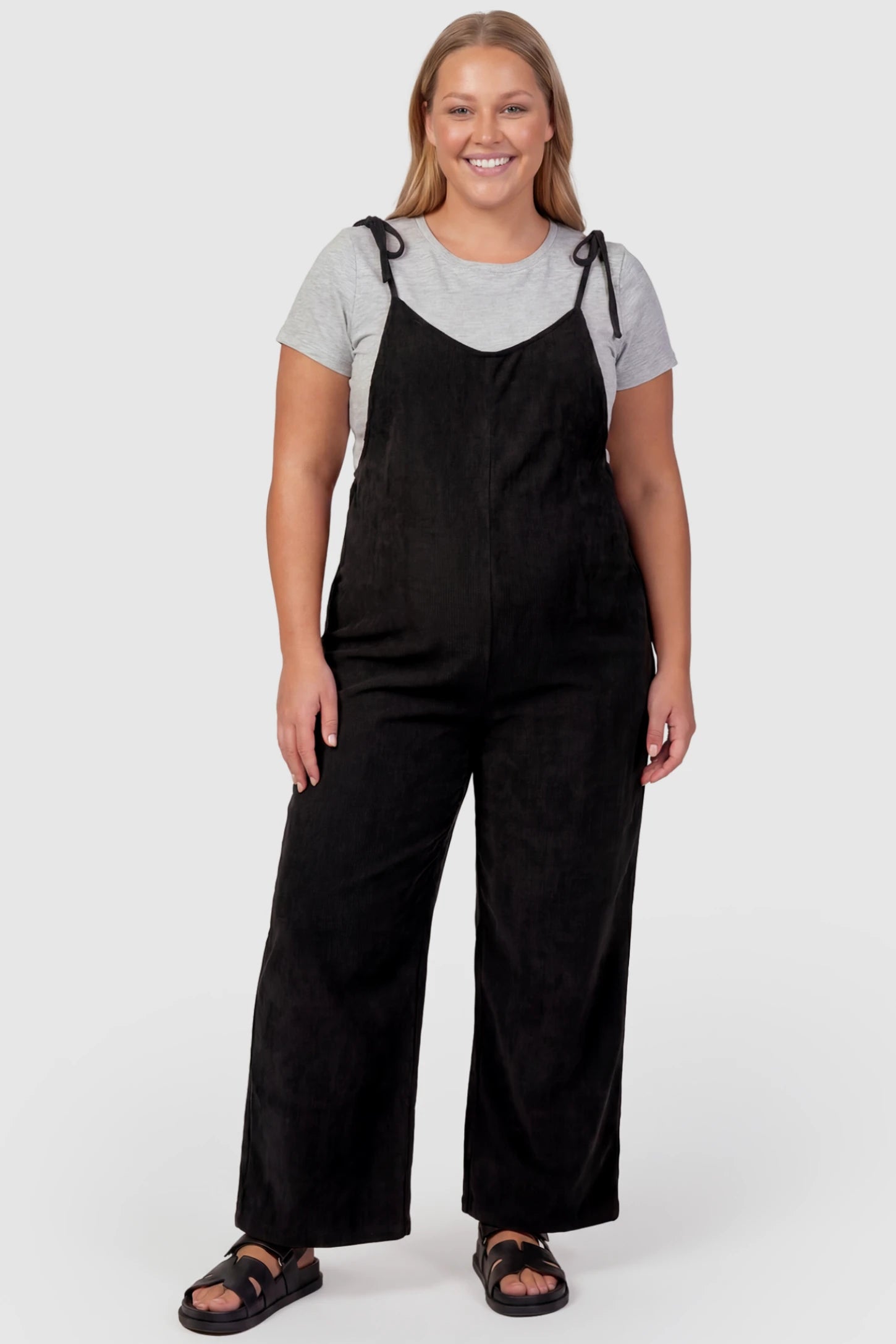 Solid Sleeveless Wide Leg Maternity Jumpsuit Solid Sleeveless Wide Leg Maternity Jumpsuit in Black featuring a flowy silhouette on a plus size pregnant model, front view.