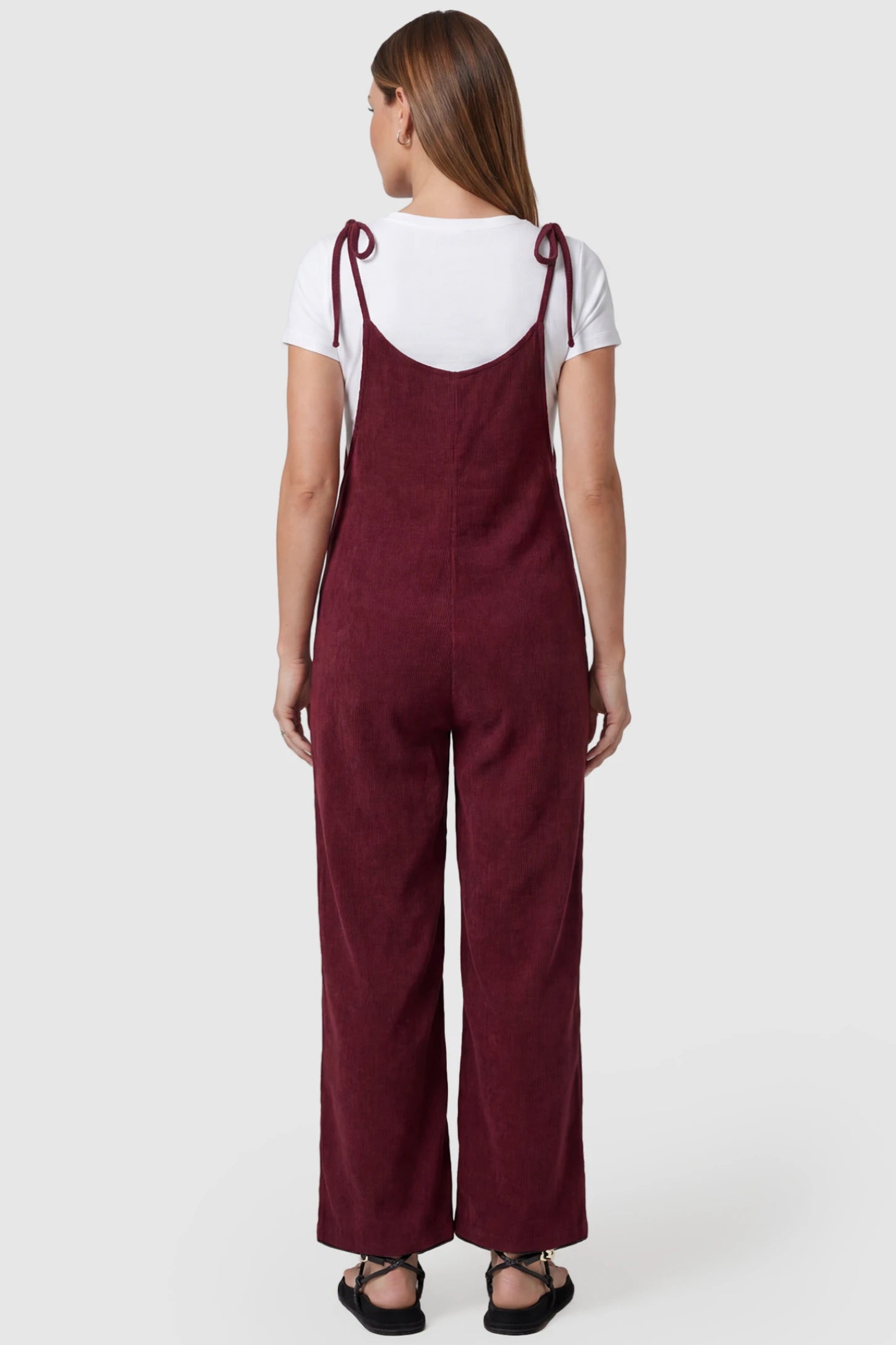Solid Sleeveless Wide Leg Maternity Jumpsuit Solid Sleeveless Wide Leg Maternity Jumpsuit in Wine Red featuring a flowy silhouette on a pregnant model, back view.
