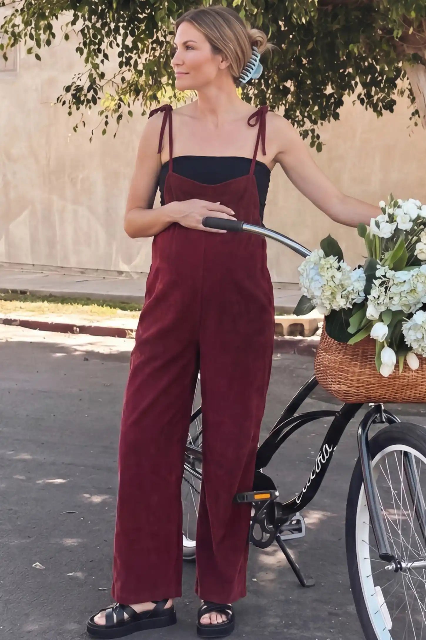 Solid Sleeveless Wide Leg Maternity Jumpsuit Solid Sleeveless Wide Leg Maternity Jumpsuit in Wine Red featuring a flowy silhouette on a pregnant woman in an outdoor setting, front view.