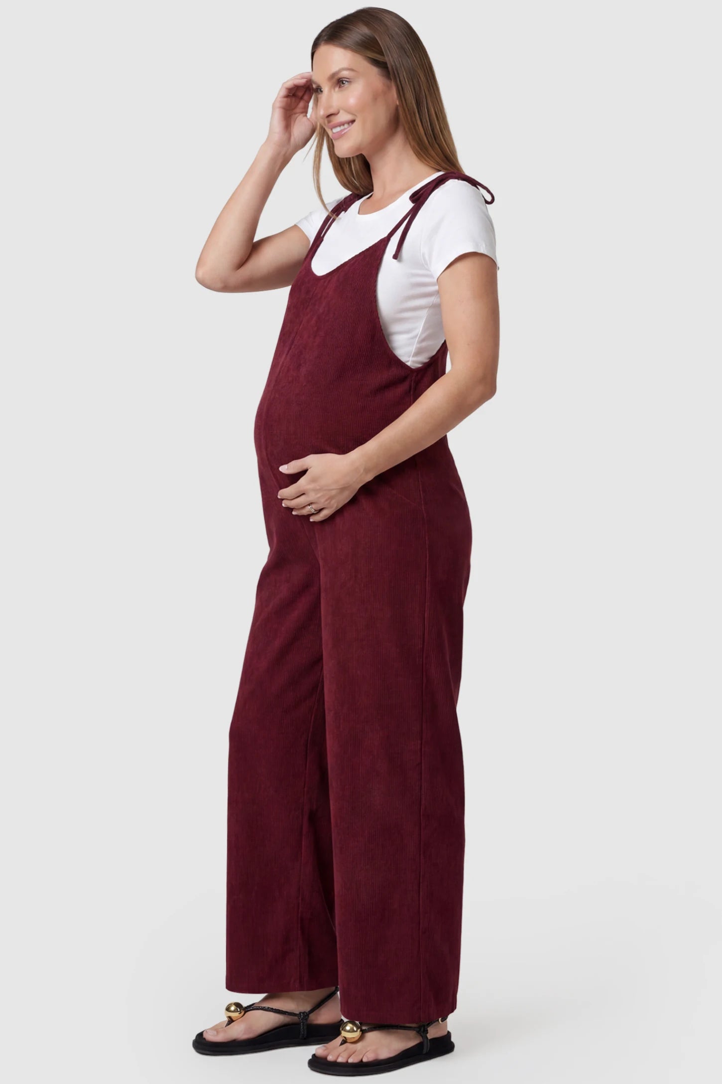 Solid Sleeveless Wide Leg Maternity Jumpsuit Solid Sleeveless Wide Leg Maternity Jumpsuit in Wine Red featuring a flowy silhouette on a pregnant model, side view.