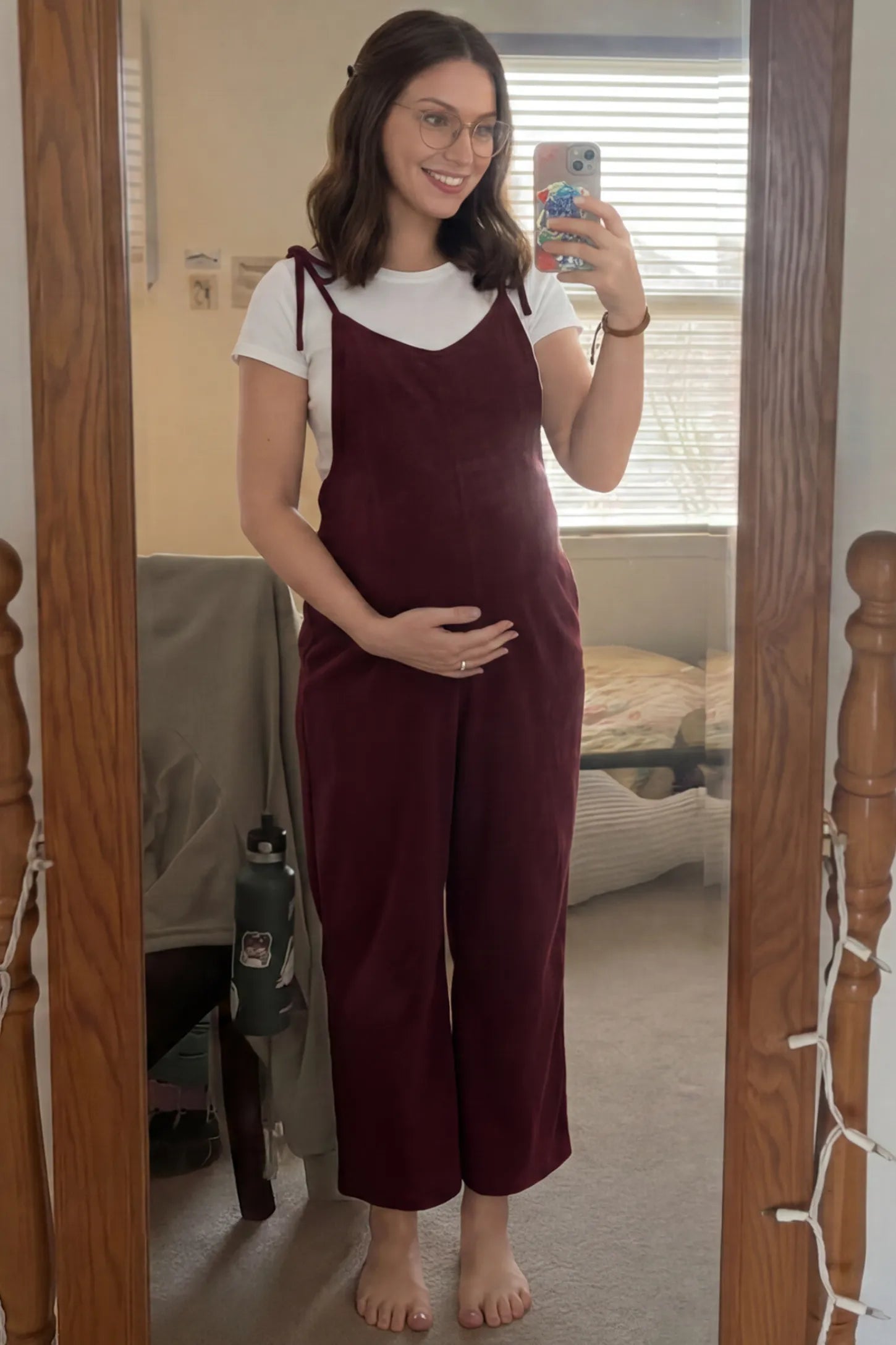 Solid Sleeveless Wide Leg Maternity Jumpsuit Solid Sleeveless Wide Leg Maternity Jumpsuit in Wine Red featuring a flowy silhouette on a pregnant woman in an indoor setting, front view.