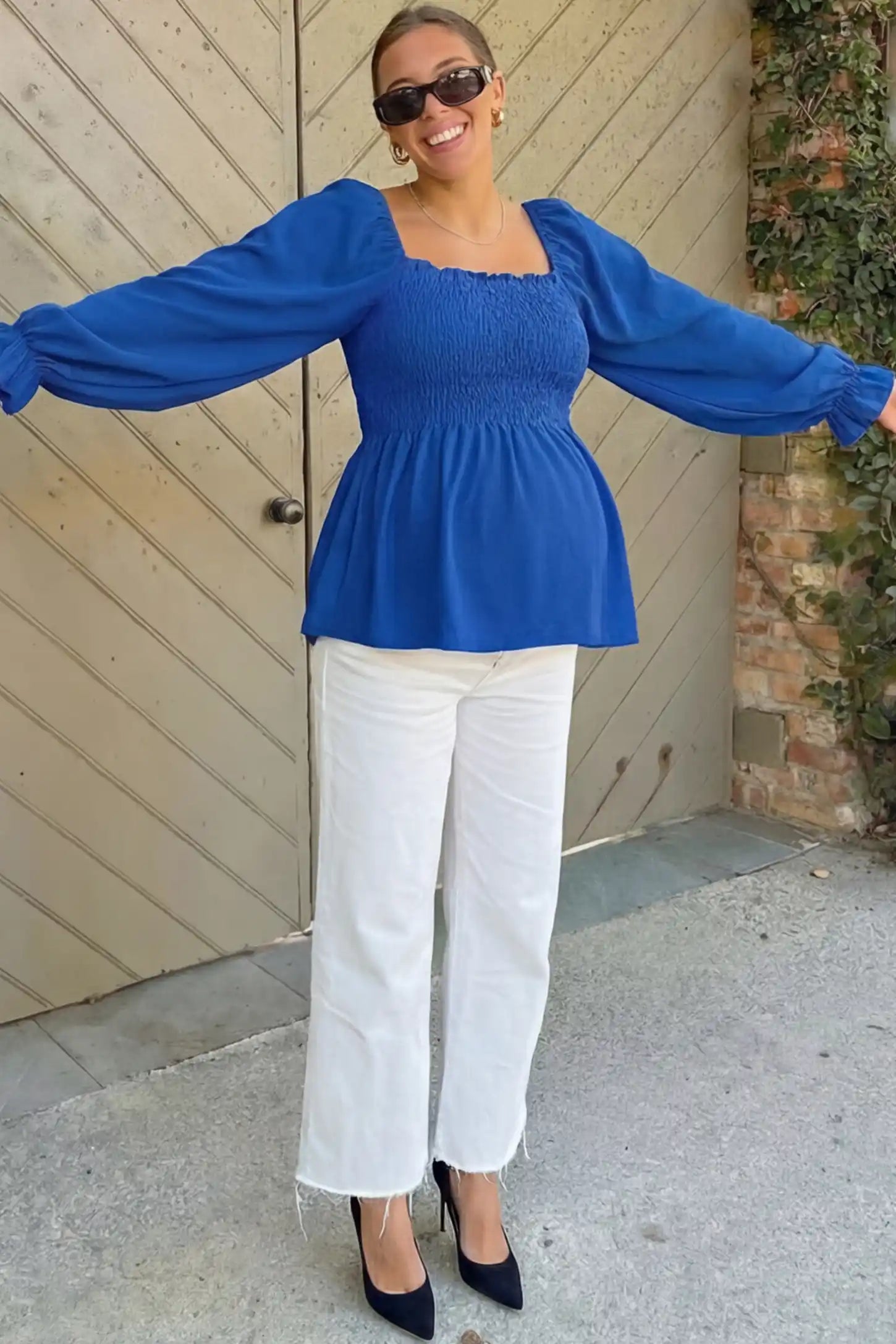 Smocked Convertible Neckline Bishop Sleeve Maternity Top Smocked Convertible Neckline Bishop Sleeve Maternity Top in Blue featuring a smocked bodice on a pregnant model in an outdoor setting, front view.