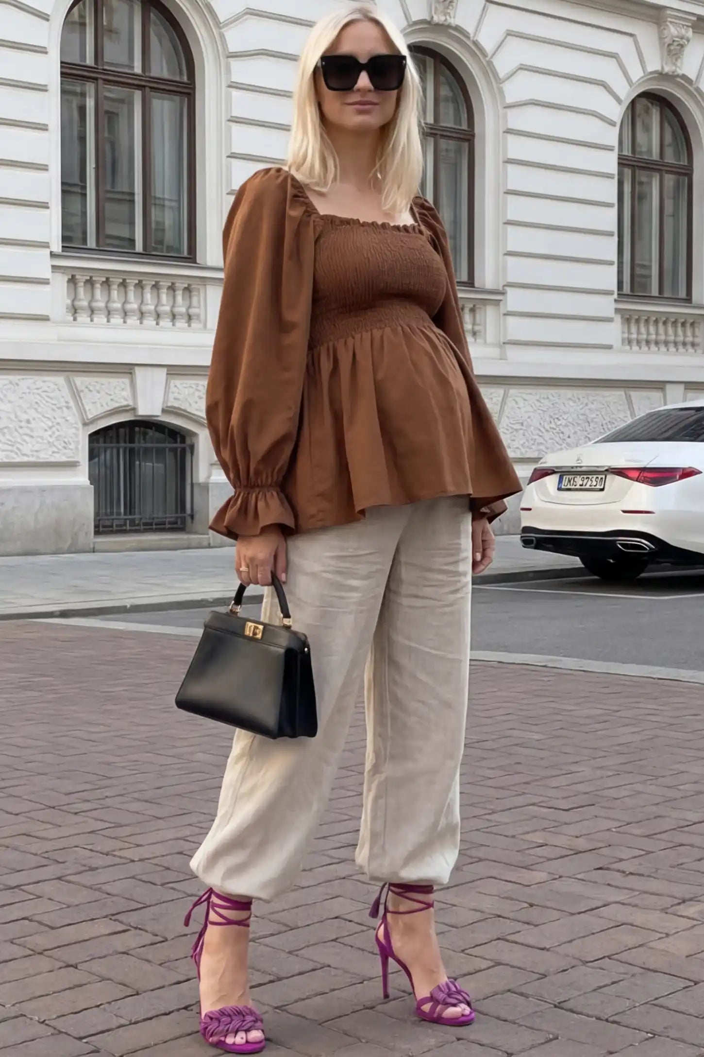 Smocked Convertible Neckline Bishop Sleeve Maternity Top Smocked Convertible Neckline Bishop Sleeve Maternity Top in Coffee featuring a smocked bodice on a pregnant model in an outdoor setting, front view.