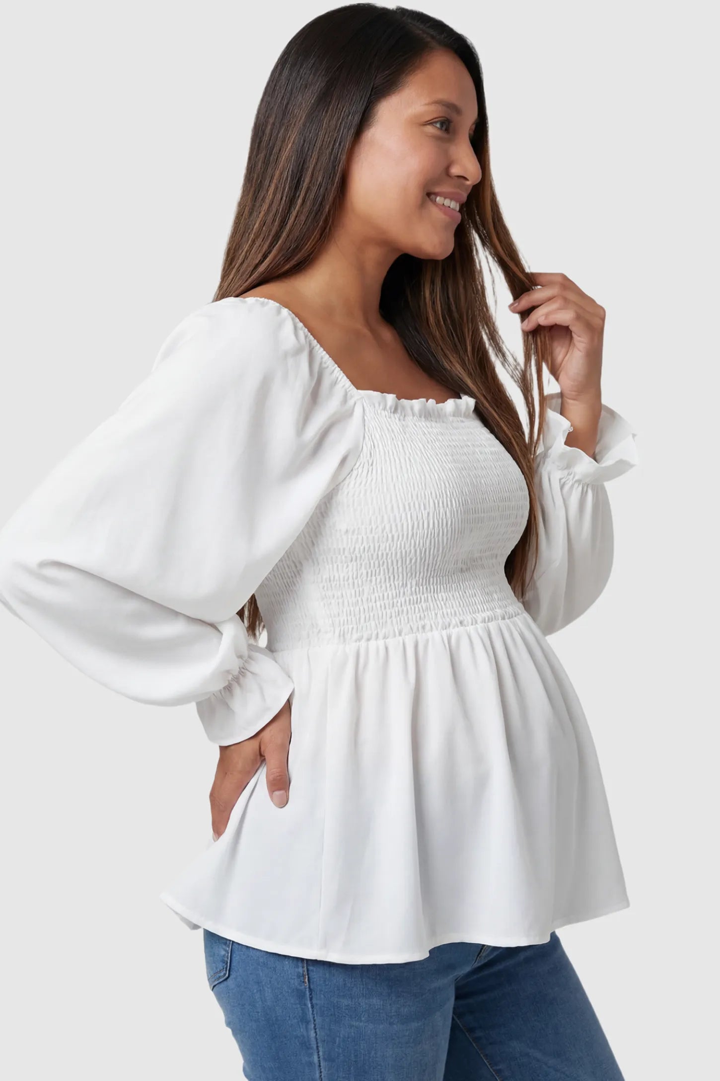 Smocked Convertible Neckline Bishop Sleeve Maternity Top Smocked Convertible Neckline Bishop Sleeve Maternity Top in White featuring a peplum hem on a pregnant model side view.