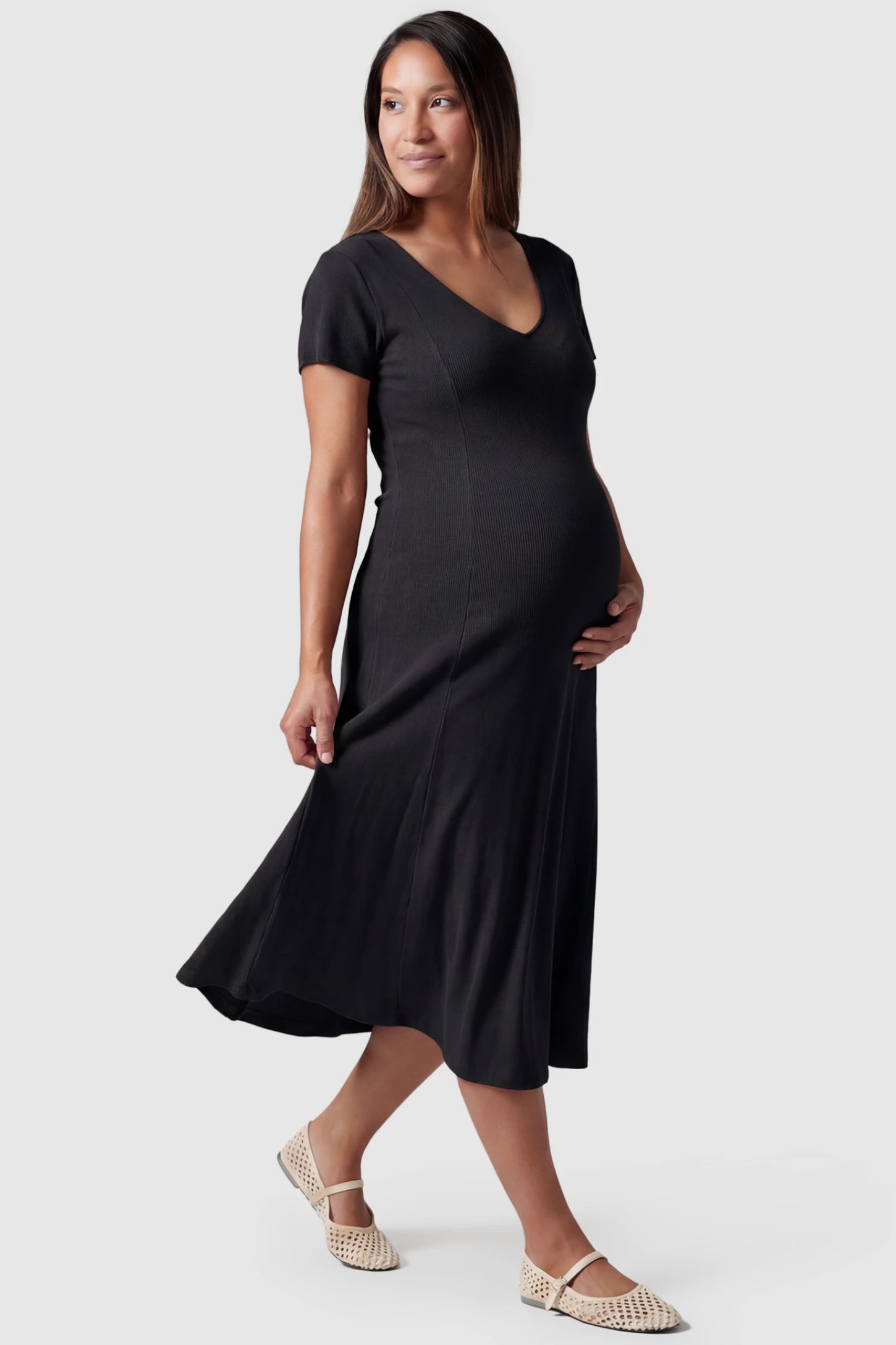 Soft Knit Stretch Short Sleeve Maternity Midi Dress Soft Knit Stretch Short Sleeve Maternity Midi Dress in Black featuring a flattering v-neck and high stretch knit on a pregnant model, side view.