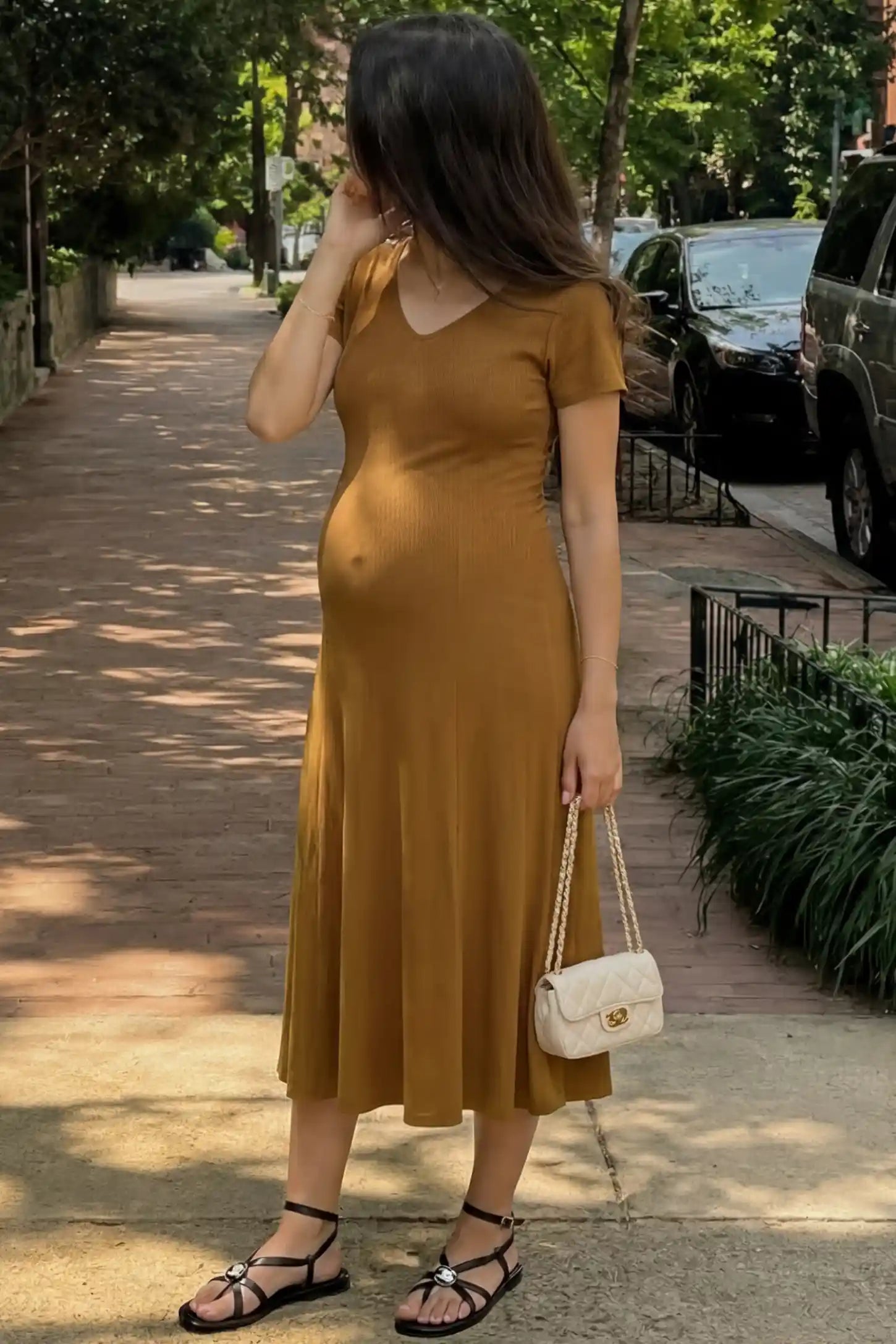 Soft Knit Stretch Short Sleeve Maternity Midi Dress Soft Knit Stretch Short Sleeve Maternity Midi Dress in Camel featuring a flattering v-neck and high stretch knit on a pregnant woman walking down a city sidewalk.
