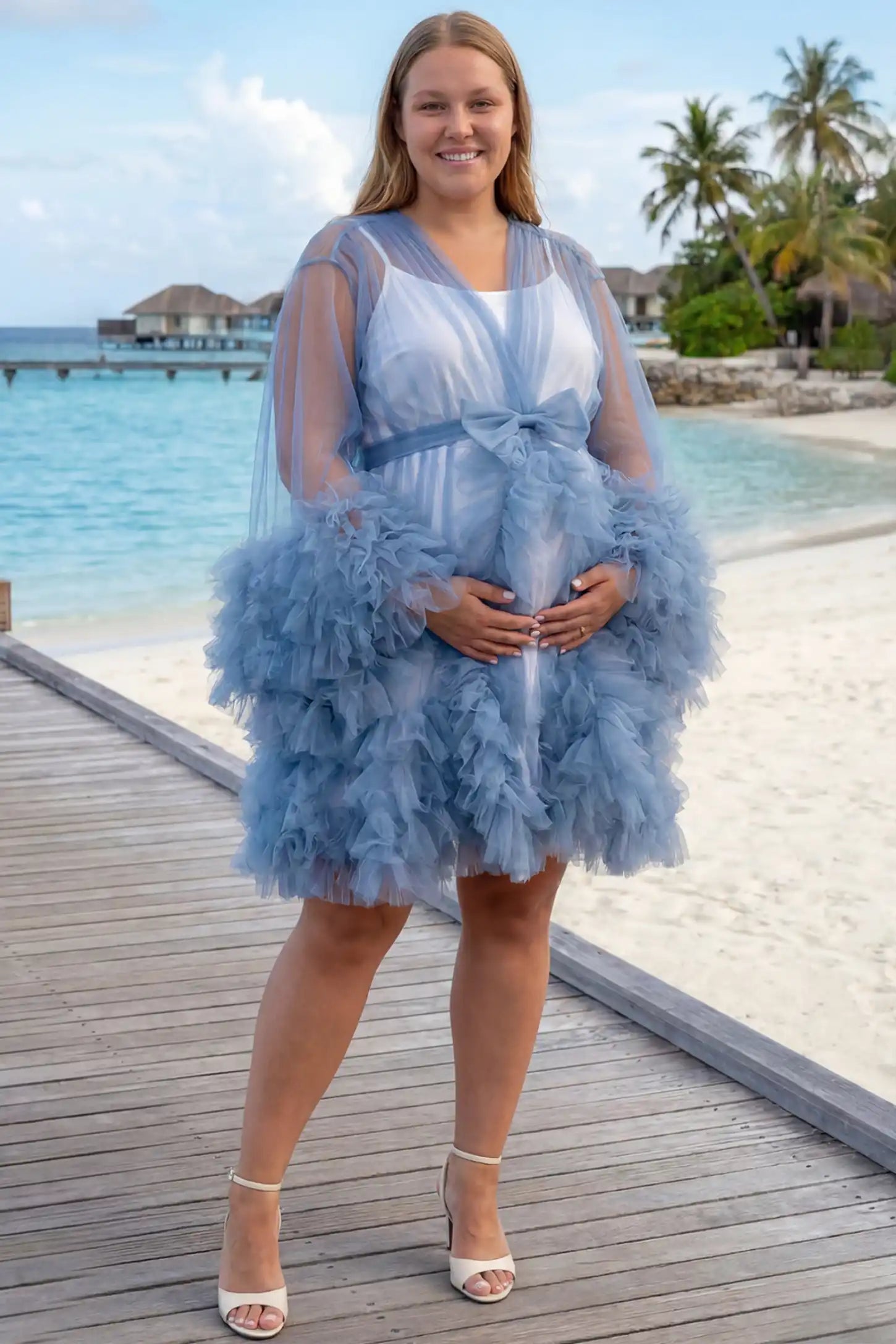 Soft Nylon Mesh Long Sleeve Maternity Photoshoot Dress Soft Nylon Mesh Long Sleeve Maternity Photoshoot Dress in Blue featuring sheer V-neck, ruffle trim layered hem on a pregnant model on a beach dock, front view.