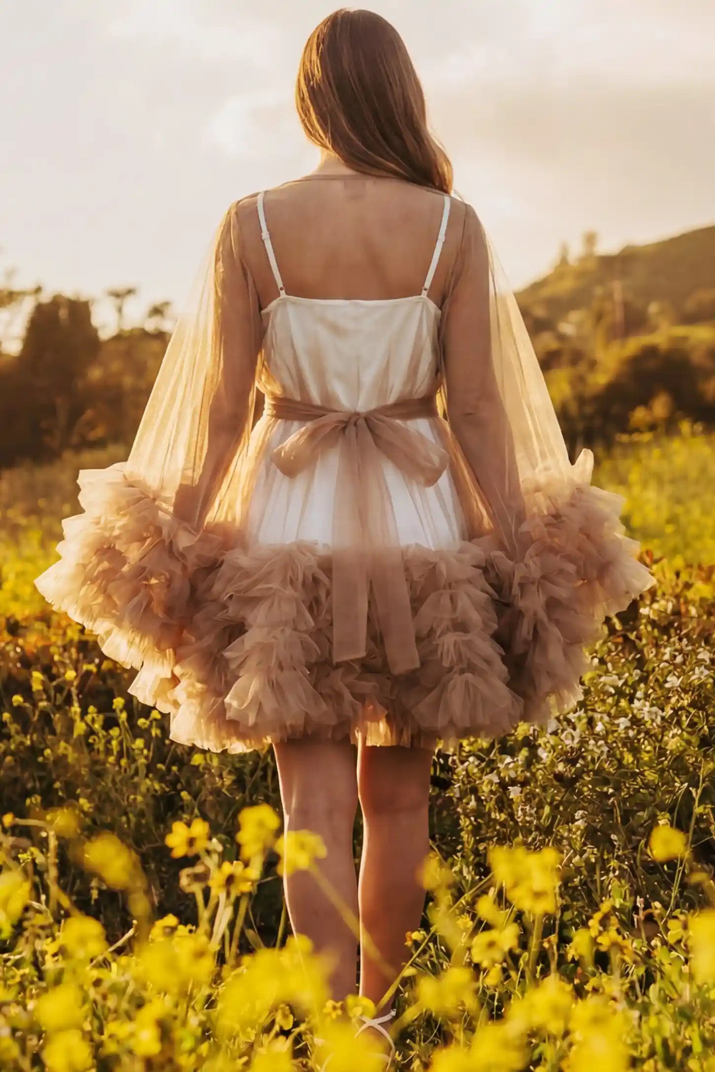 Soft Nylon Mesh Long Sleeve Maternity Photoshoot Dress Soft Nylon Mesh Long Sleeve Maternity Photoshoot Dress in Camel featuring a tied bow waist on a pregnant model in a wildflower field, back view.