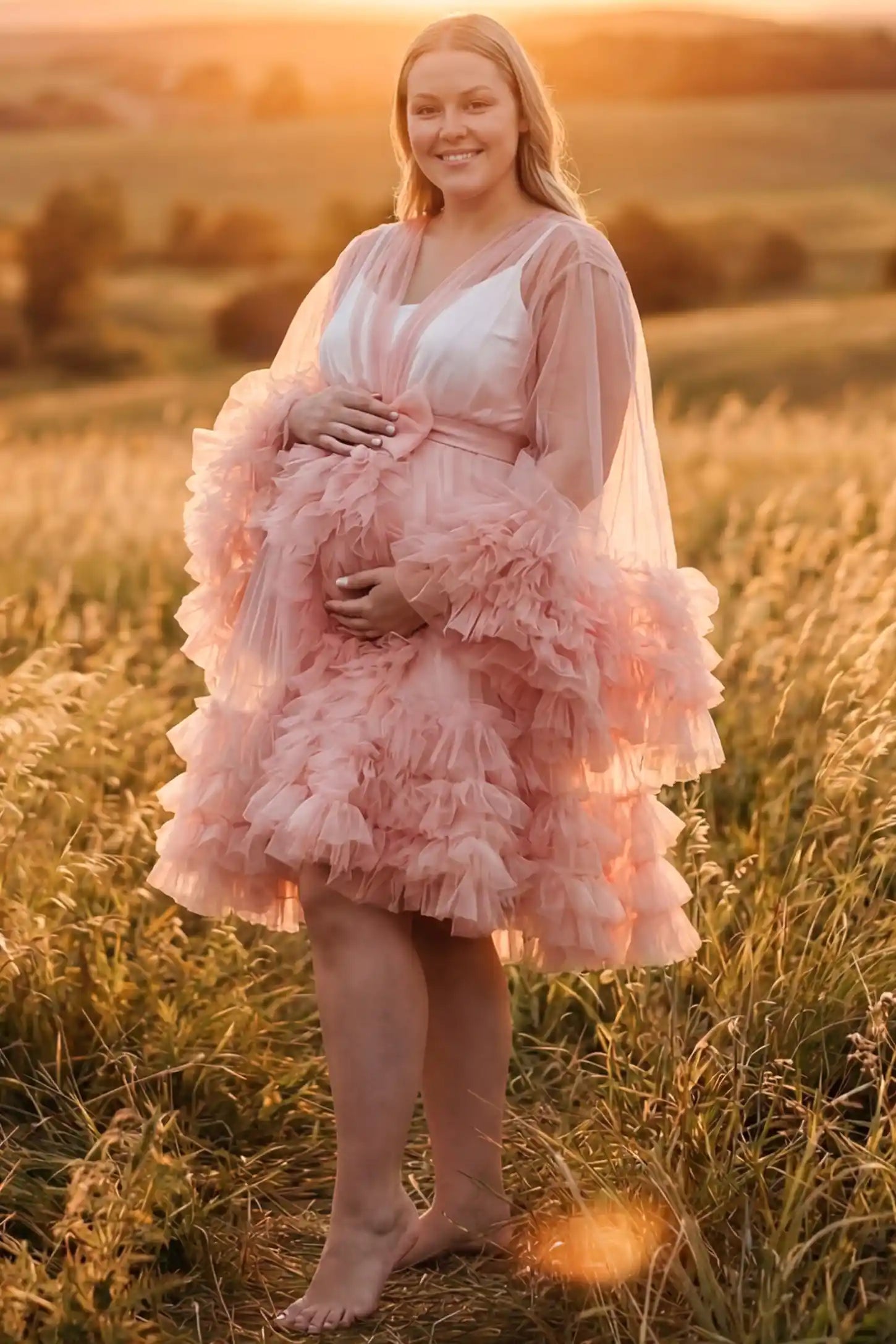 Soft Nylon Mesh Long Sleeve Maternity Photoshoot Dress Soft Nylon Mesh Long Sleeve Maternity Photoshoot Dress in Pink featuring sheer V-neck, ruffle trim layered hem on a plus size pregnant model at golden hour, front view.