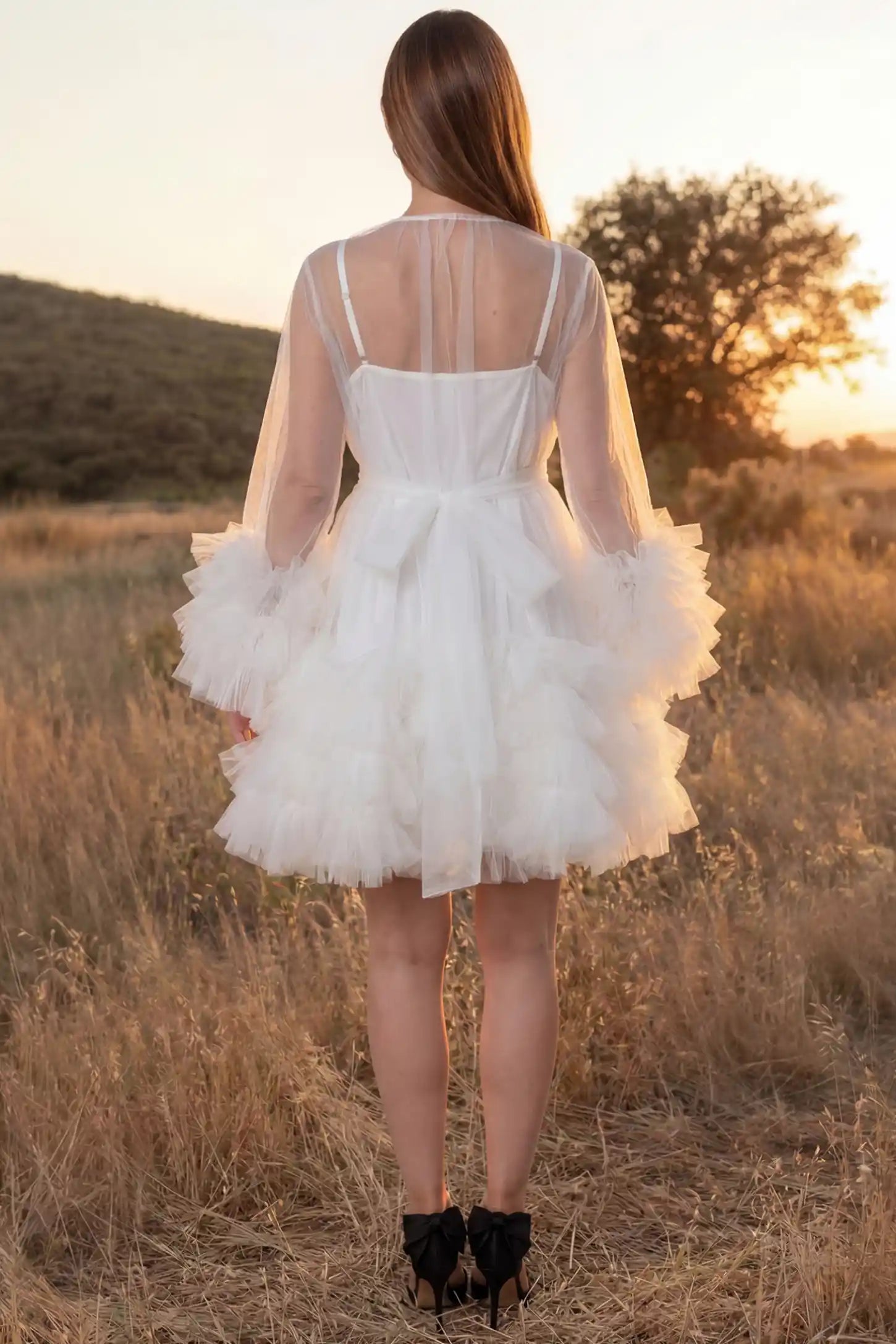 Soft Nylon Mesh Long Sleeve Maternity Photoshoot Dress Soft Nylon Mesh Long Sleeve Maternity Photoshoot Dress in White featuring a tied bow waist on a pregnant model in a golden field, back view.