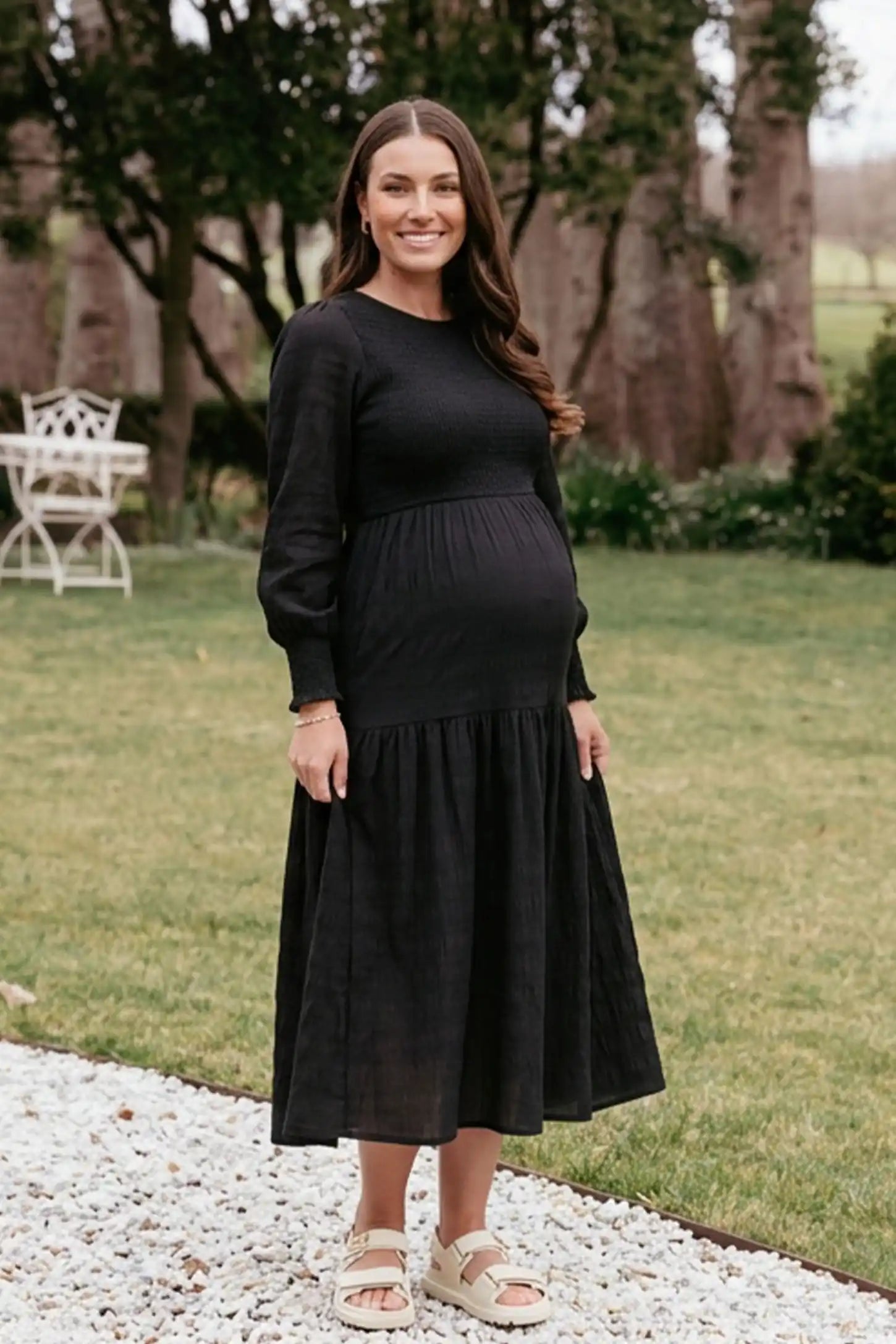 Solid Color Tiered Style Midi Maternity Dress in black featuring a smocked bodice on a pregnant model, editorial lifestyle view.