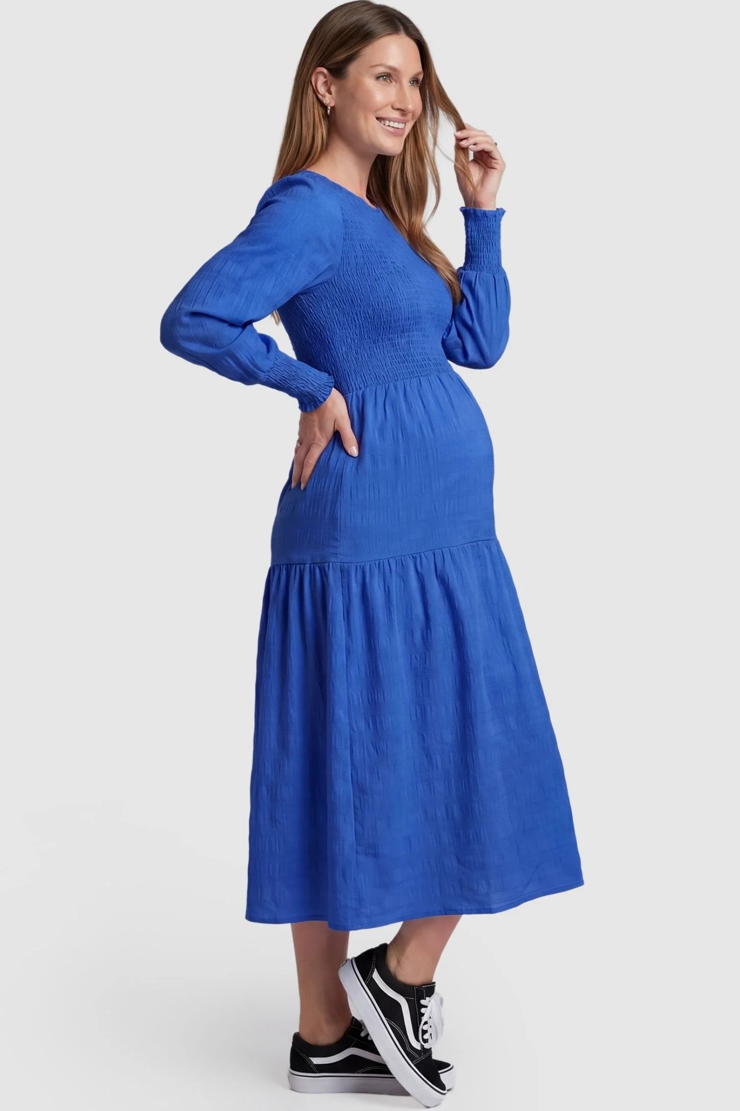 Solid Color Tiered Style Midi Maternity Dress Solid Color Tiered Style Midi Maternity Dress in blue featuring a smocked bodice on a pregnant model, side view.