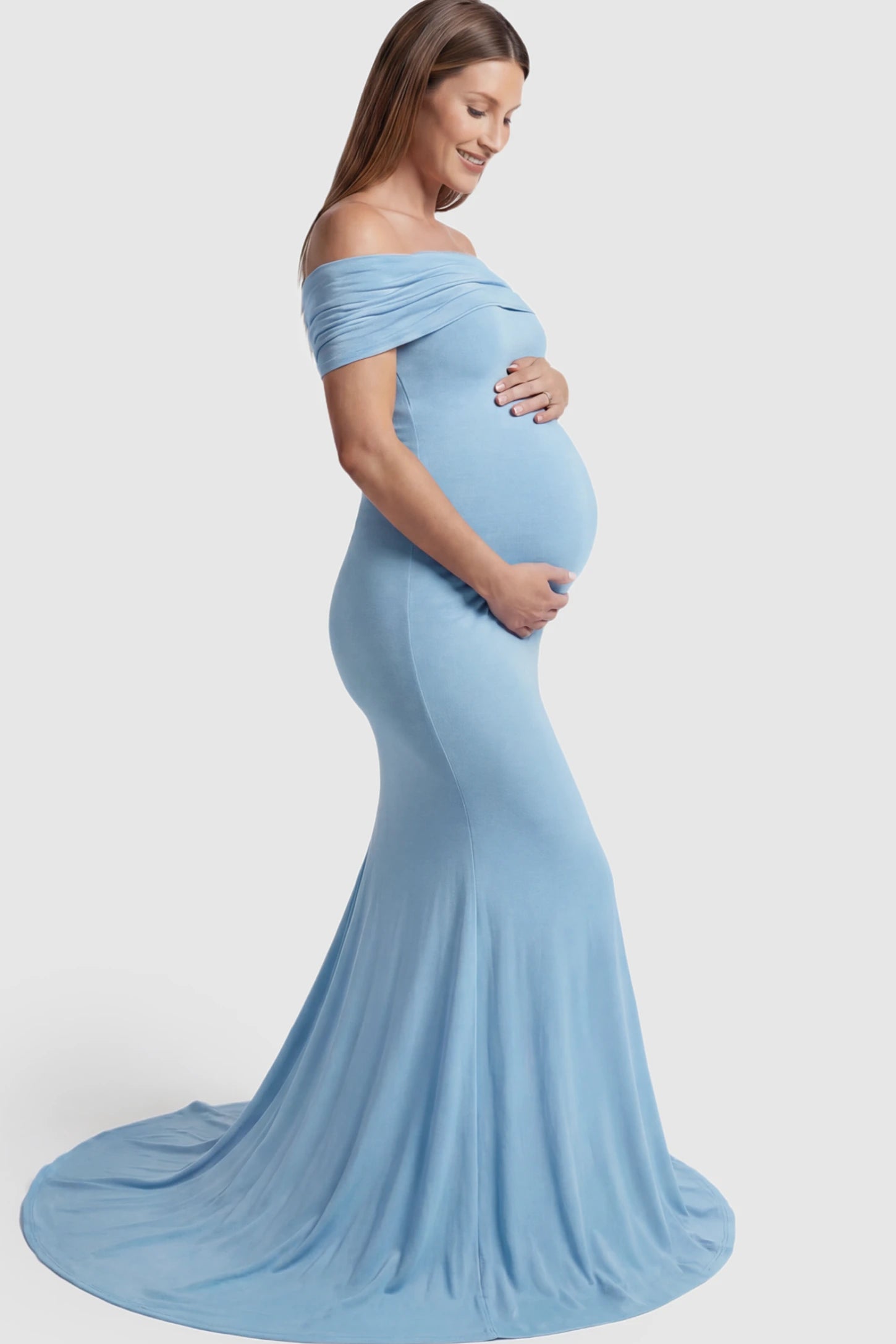 Solid Off Shoulder Maternity Photoshoot Gown Solid Off-Shoulder Maternity Photoshoot Gown in light blue featuring subtle train on a pregnant model showing side.