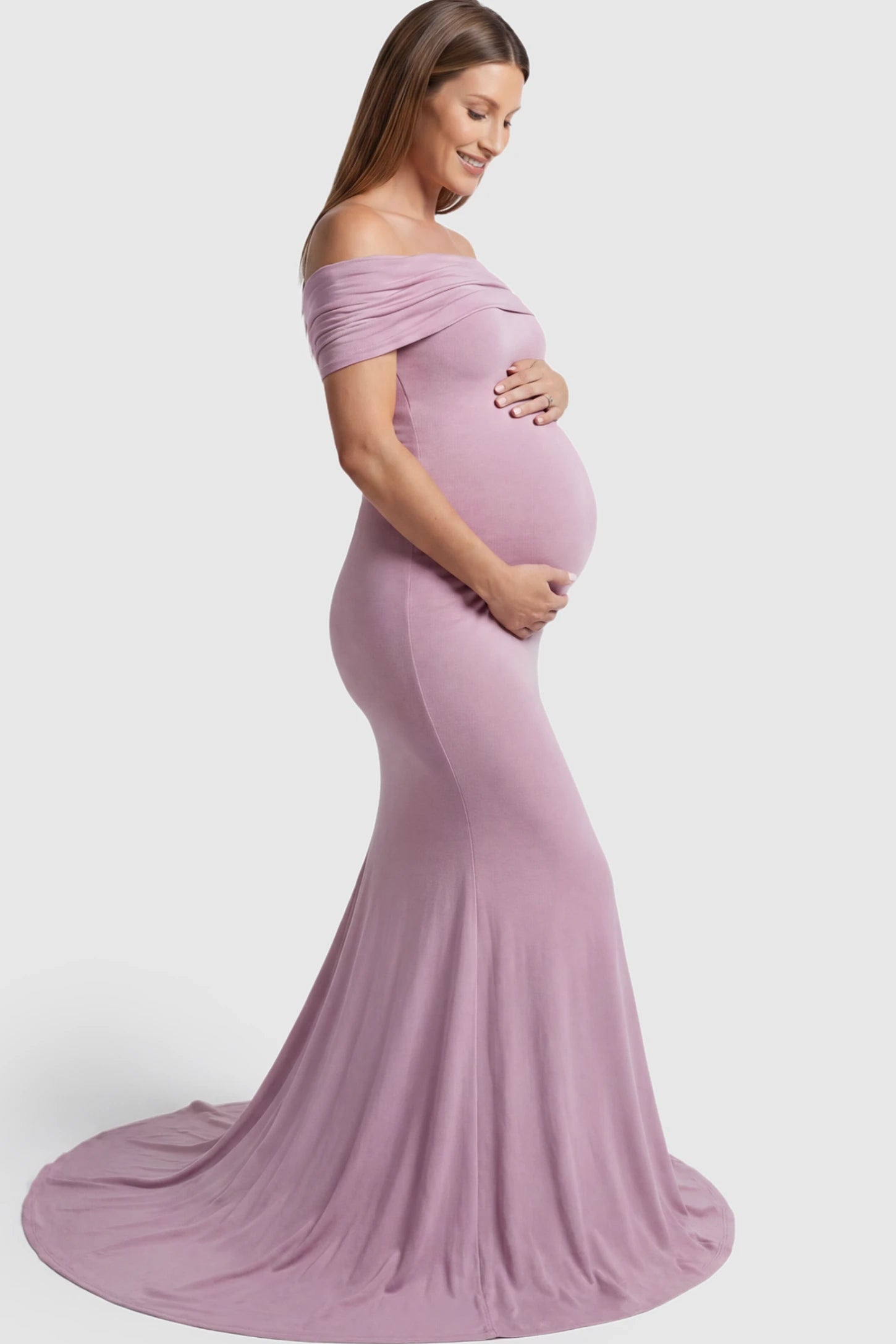 Solid Off Shoulder Maternity Photoshoot Gown Solid Off-Shoulder Maternity Photoshoot Gown in Pink featuring subtle train on a pregnant model showing side.