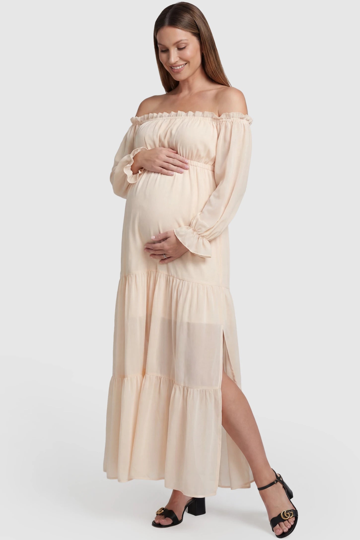 Solid Off Shoulder Tiered Maternity Maxi Dress in beige featuring flowy tiered silhouette, Long Sleeve on a pregnant model, front view.