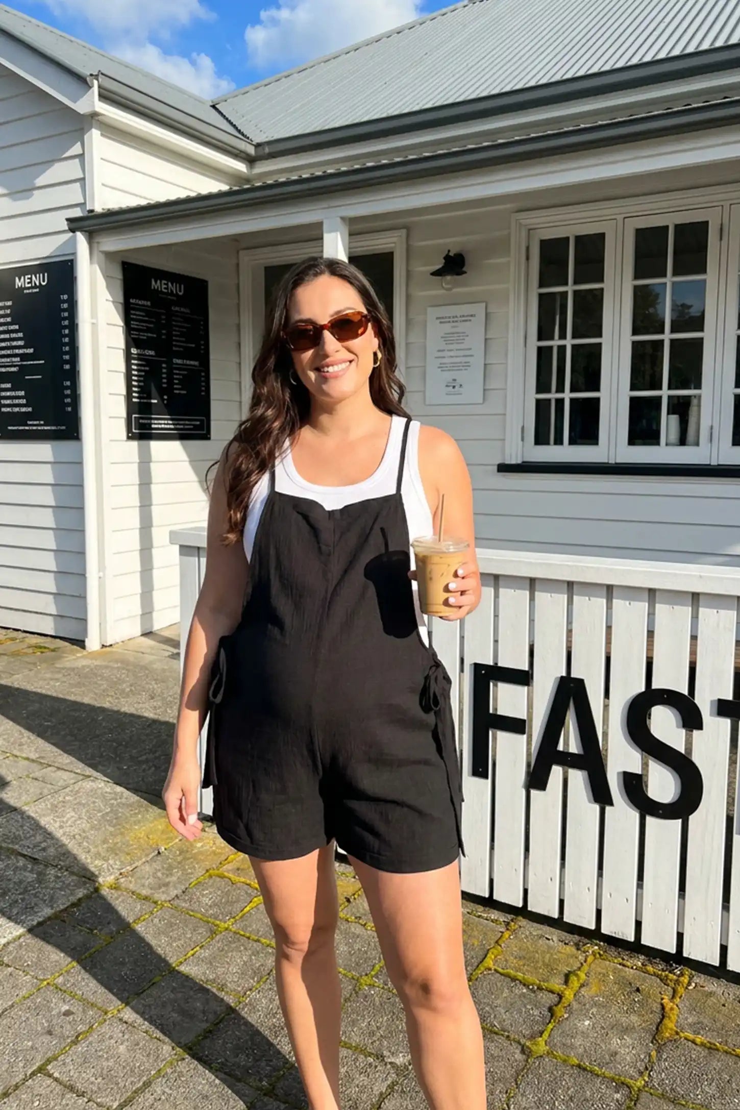 Spaghetti Strap Tie-Side Maternity Romper Model wearing the black Spaghetti Strap Tie-Side Maternity Romper in an outdoor lifestyle setting with a casual summer look.