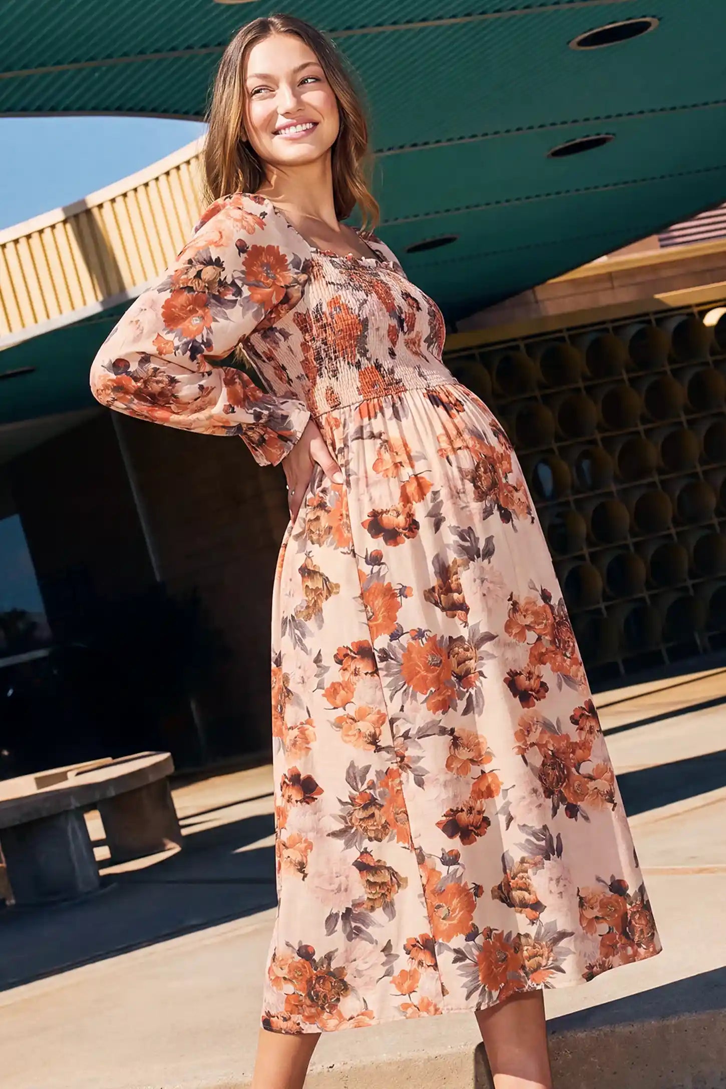 Square Neck Smocked Floral Maternity Midi Dress Square Neck Smocked Floral Maternity Midi Dress in Rust Floral featuring a flexible smocked bodice accommodating a growing bump on a pregnant model, lifestyle side view.