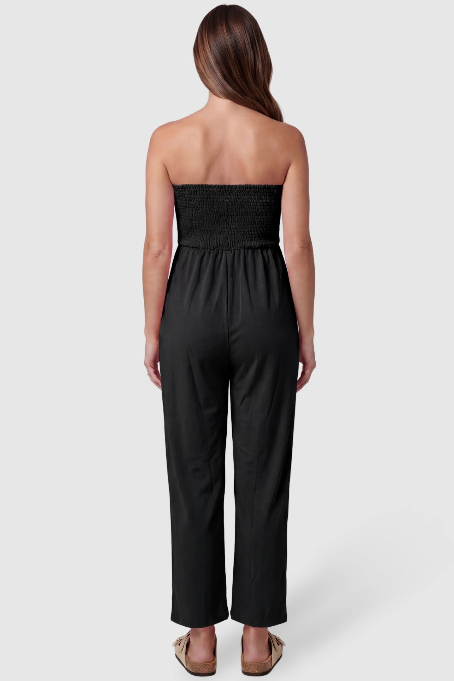Strapless Smocked Bust Wide Leg Maternity Jumpsuit Strapless Smocked Bust Wide Leg Maternity Jumpsuit in Black featuring a relaxed leg design on a pregnant model, back view.