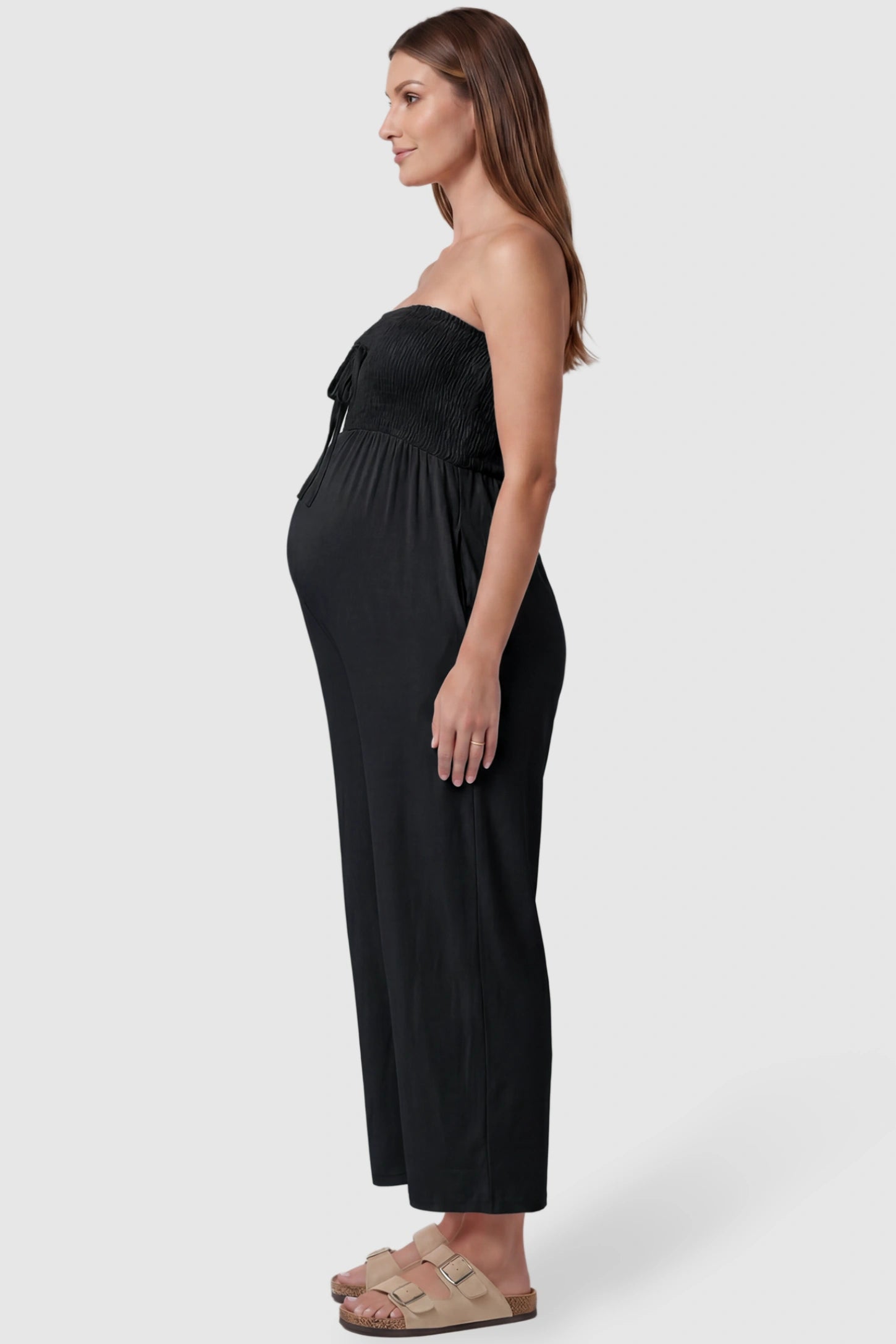 Strapless Smocked Bust Wide Leg Maternity Jumpsuit Strapless Smocked Bust Wide Leg Maternity Jumpsuit in Black featuring a relaxed leg design on a pregnant model, side view.